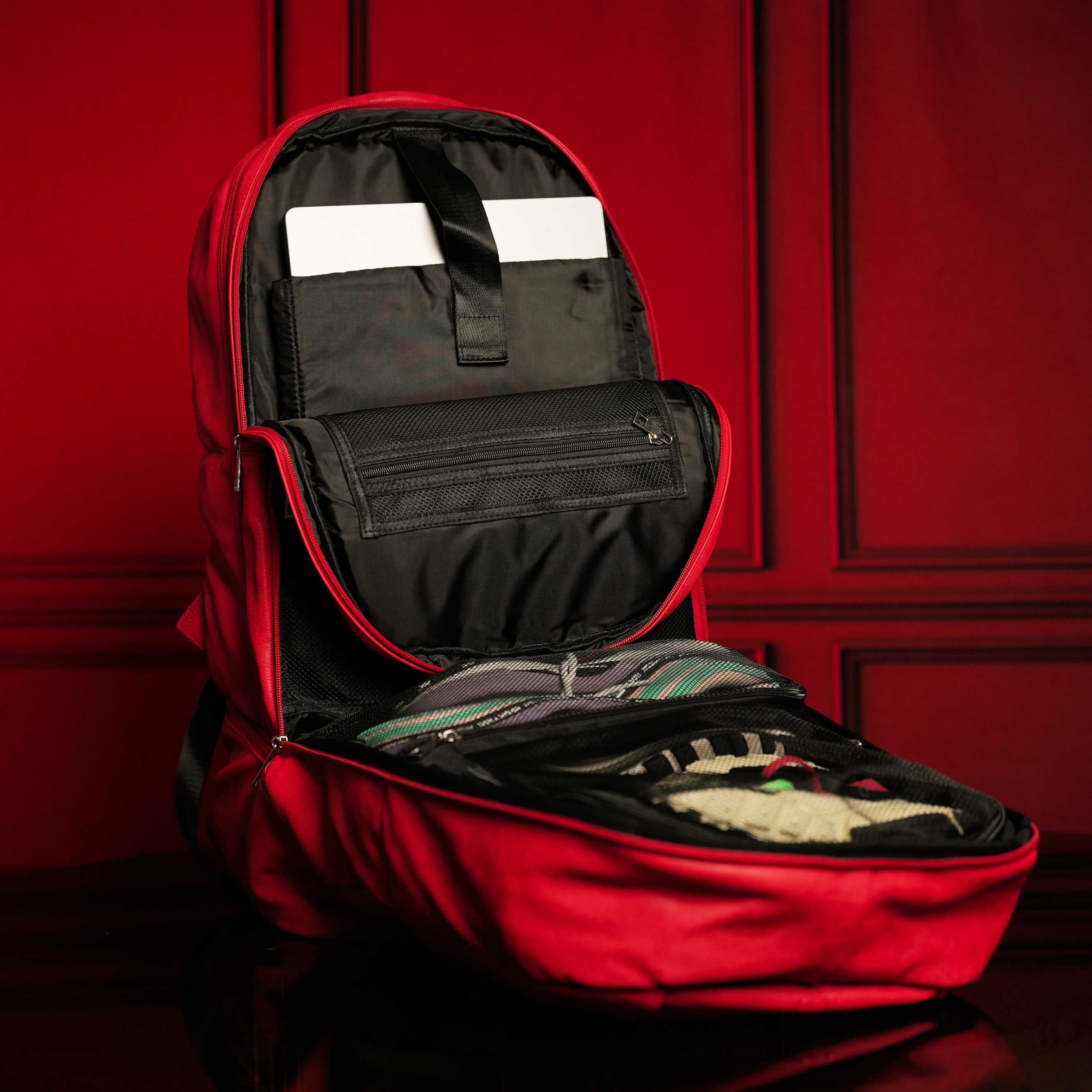 Red backpack with open compartment against a red wall