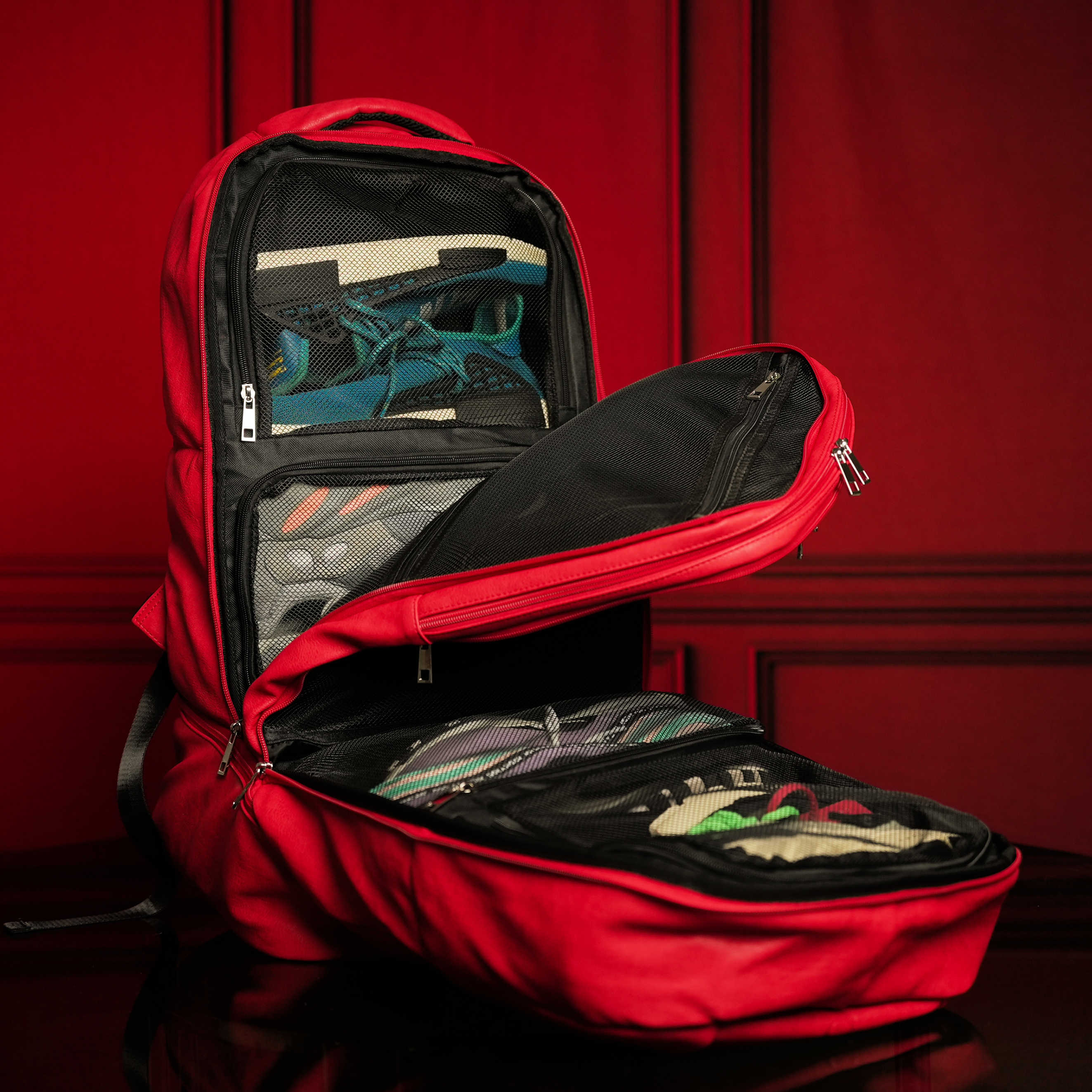Red backpack with open front compartment displaying shoes against a red background