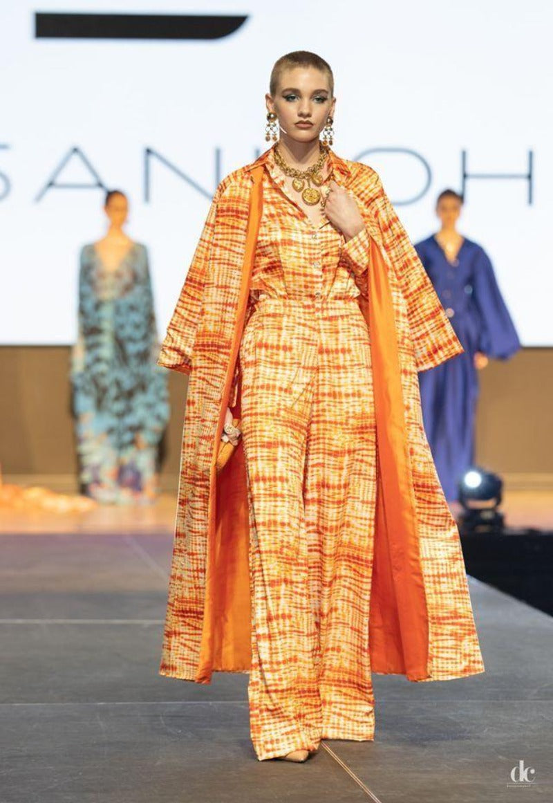 Model wearing an orange and white patterned outfit on a fashion runway with 'SANDRO' branding.