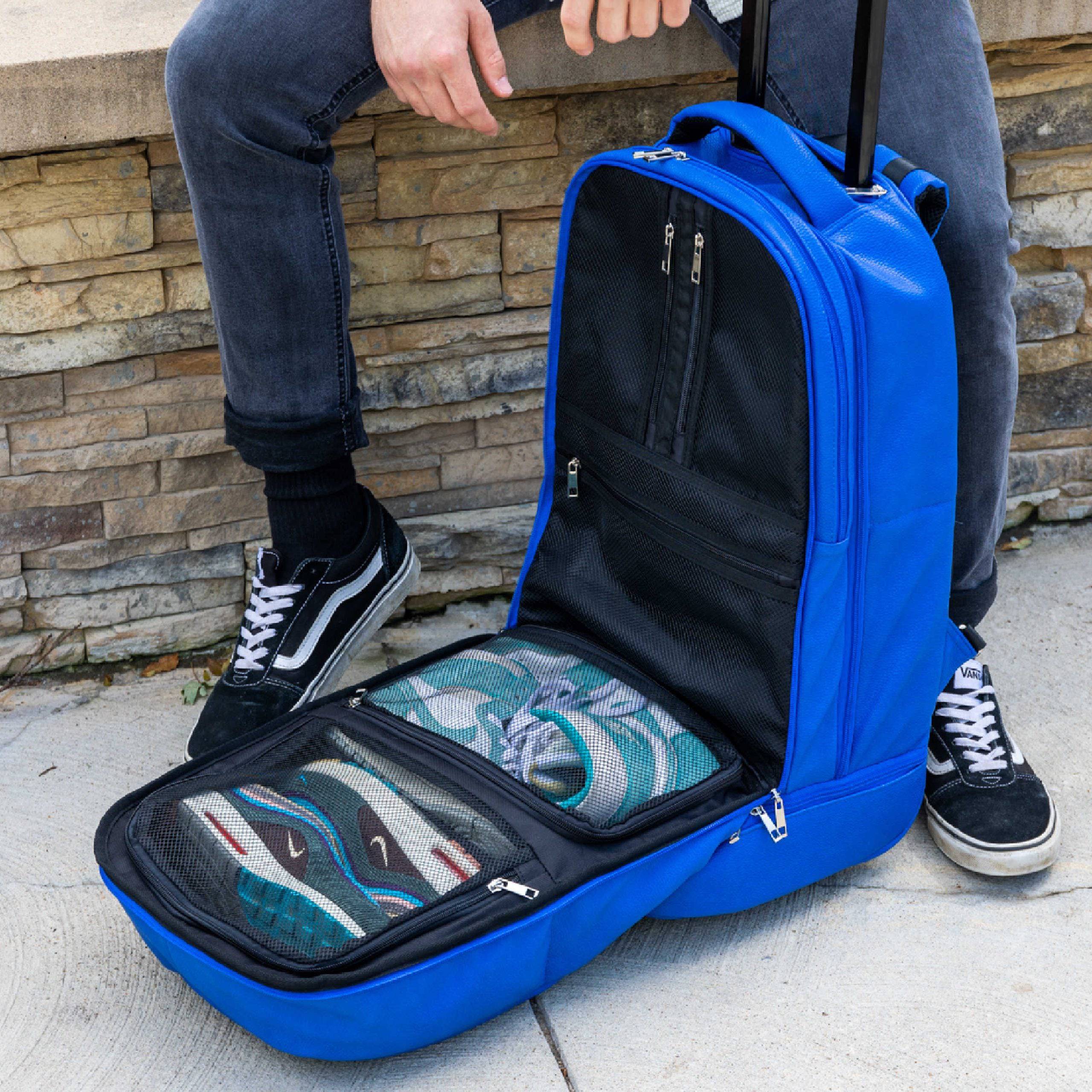 Blue suitcase with open compartment showing shoes, held by a person against a stone wall.