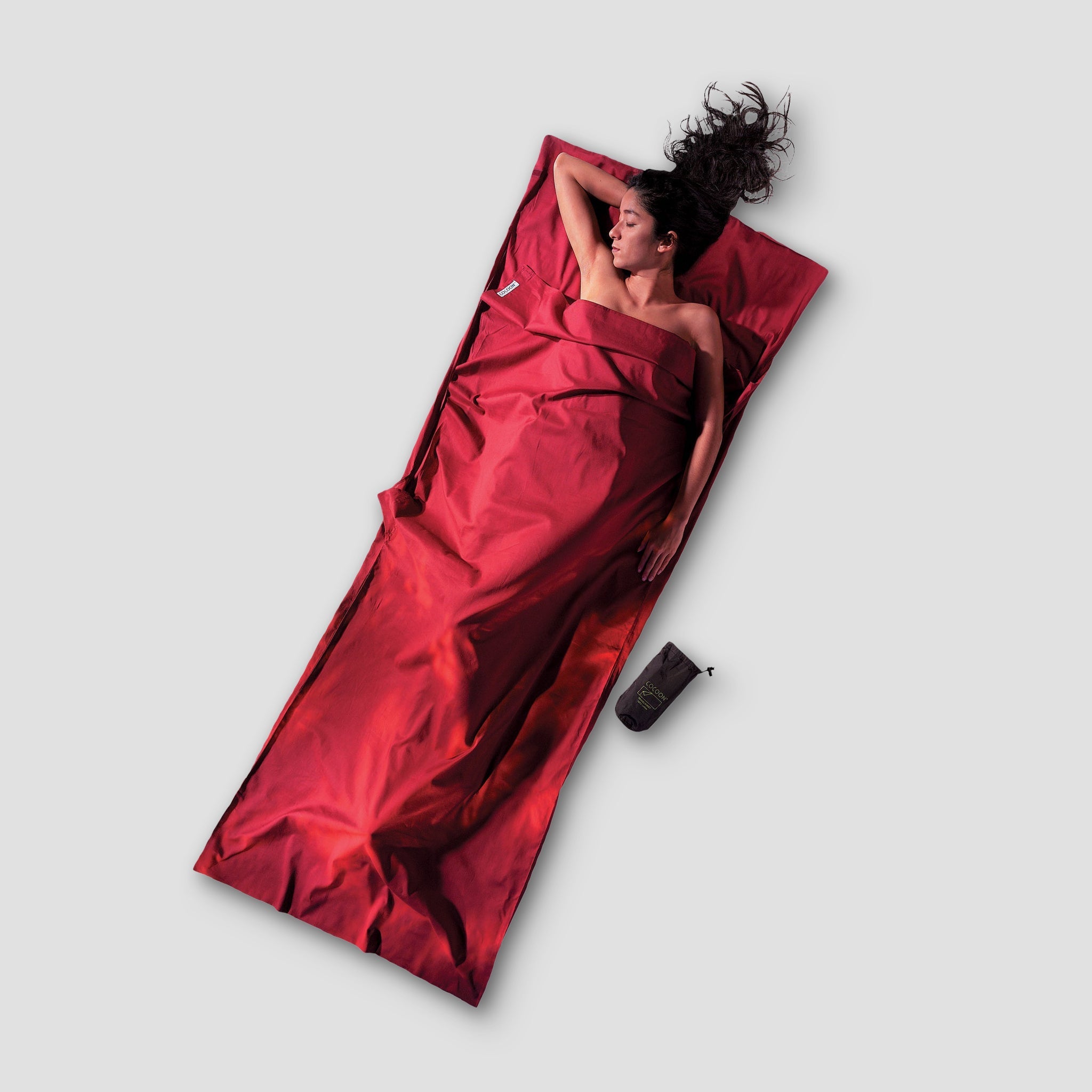 Person lying on a red sleeping bag with a gray background