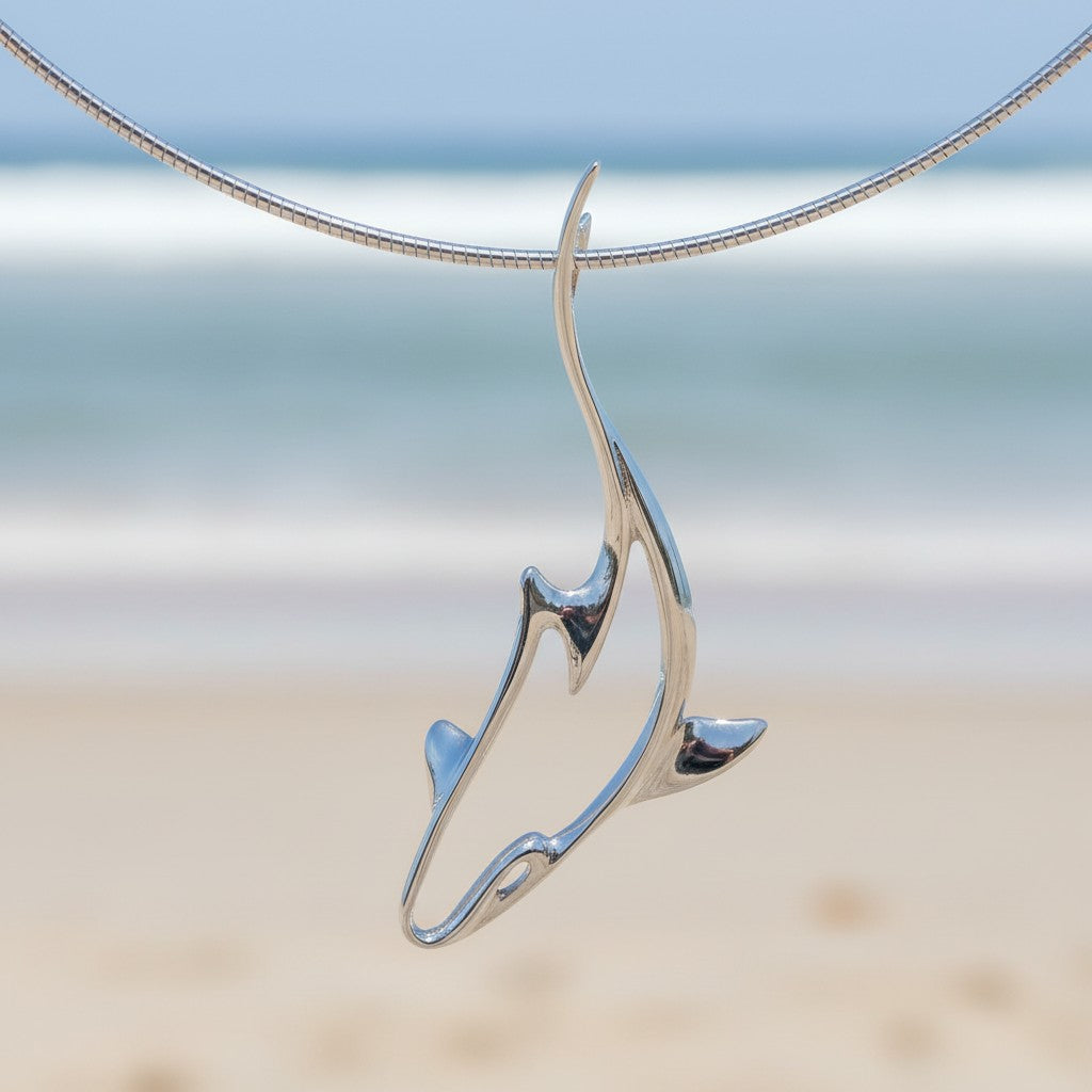 Silver necklace with a fish-shaped pendant against a blurred beach background