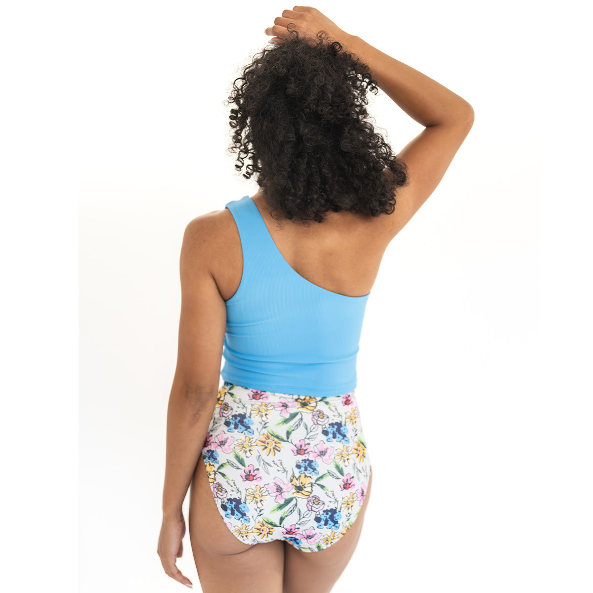 Woman wearing a blue tank top and floral high-waisted shorts on a white background