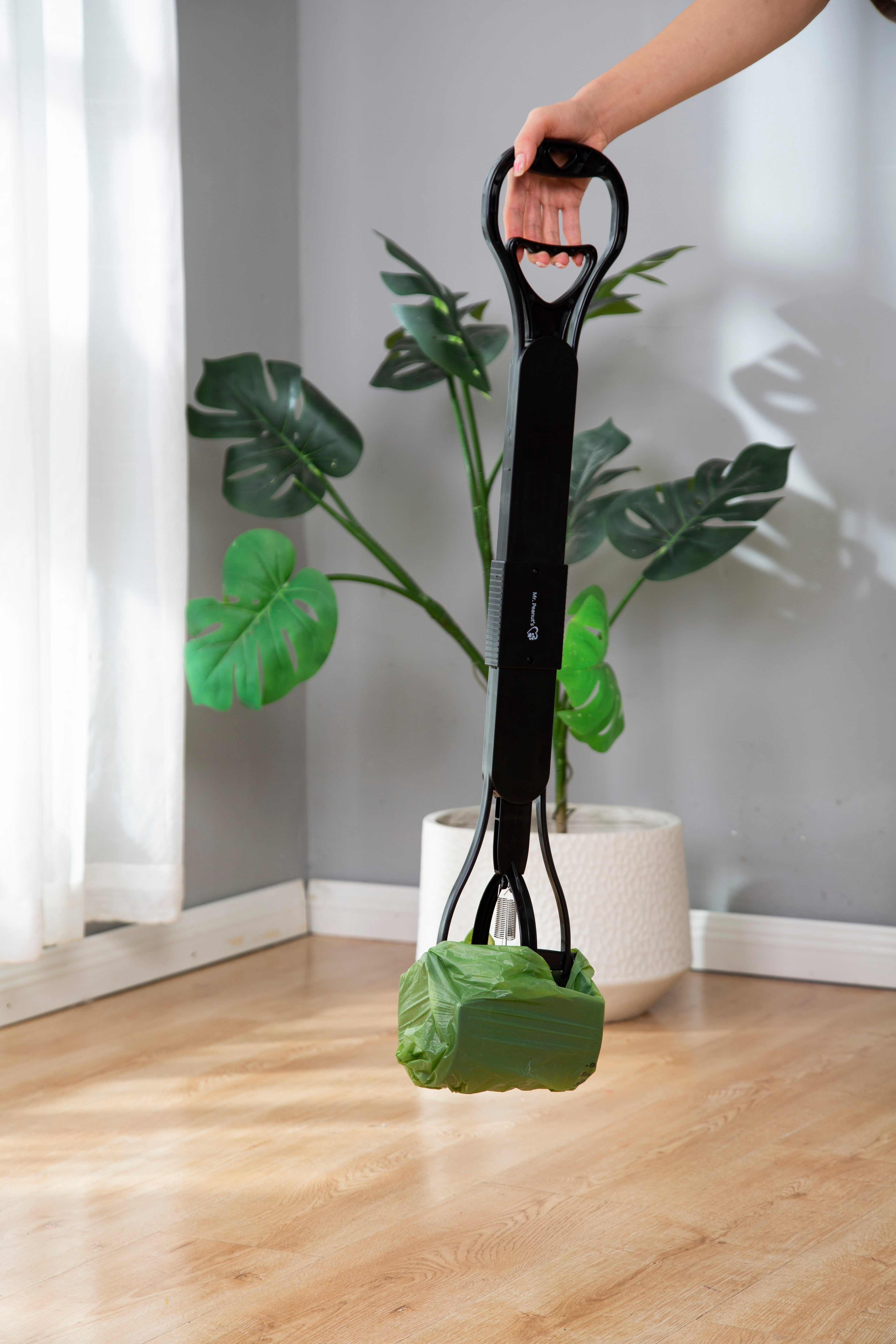 Person holding a green leaf-shaped bag with a black handle in front of a plant.