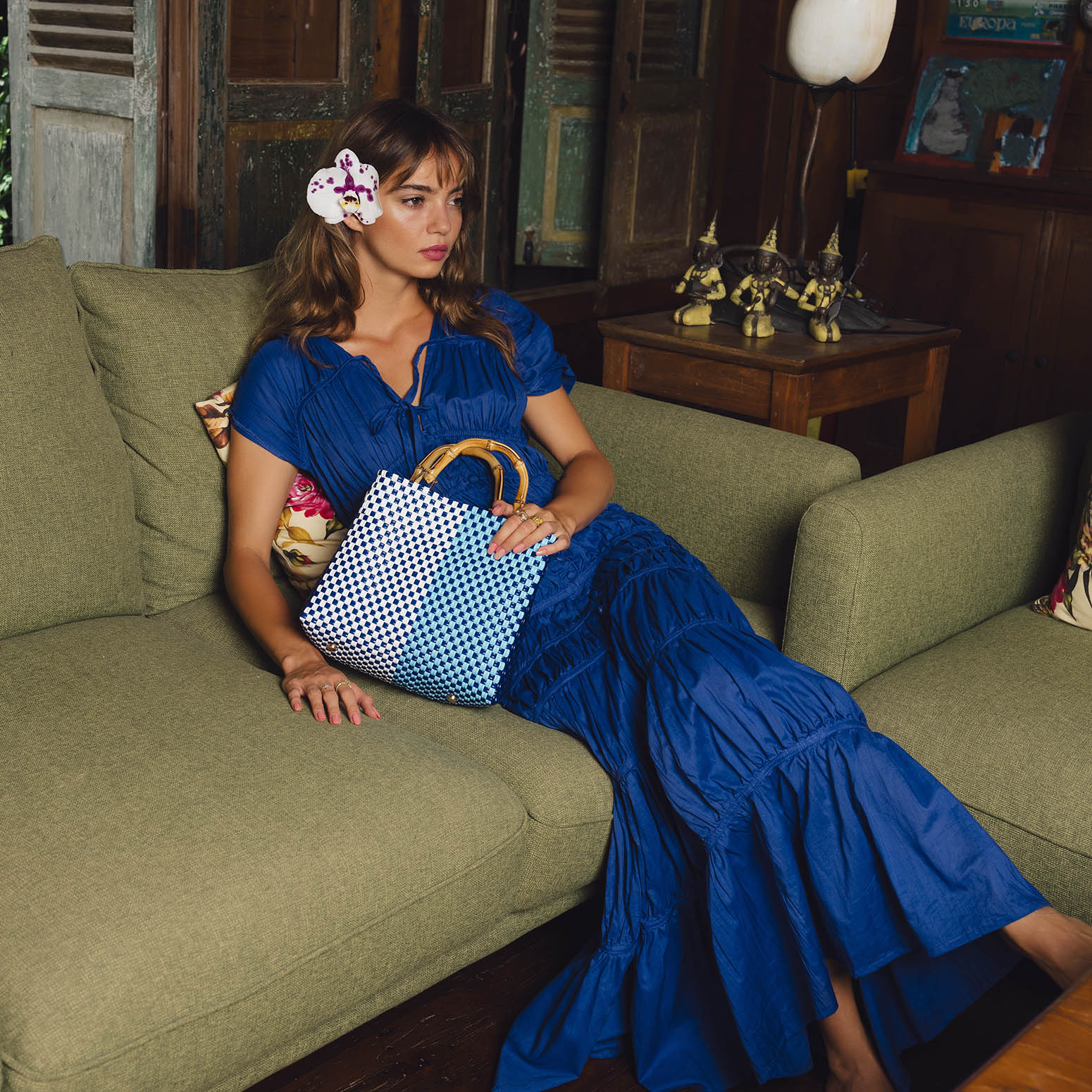 Woman in a blue dress sitting on a green couch holding a checkered bag.