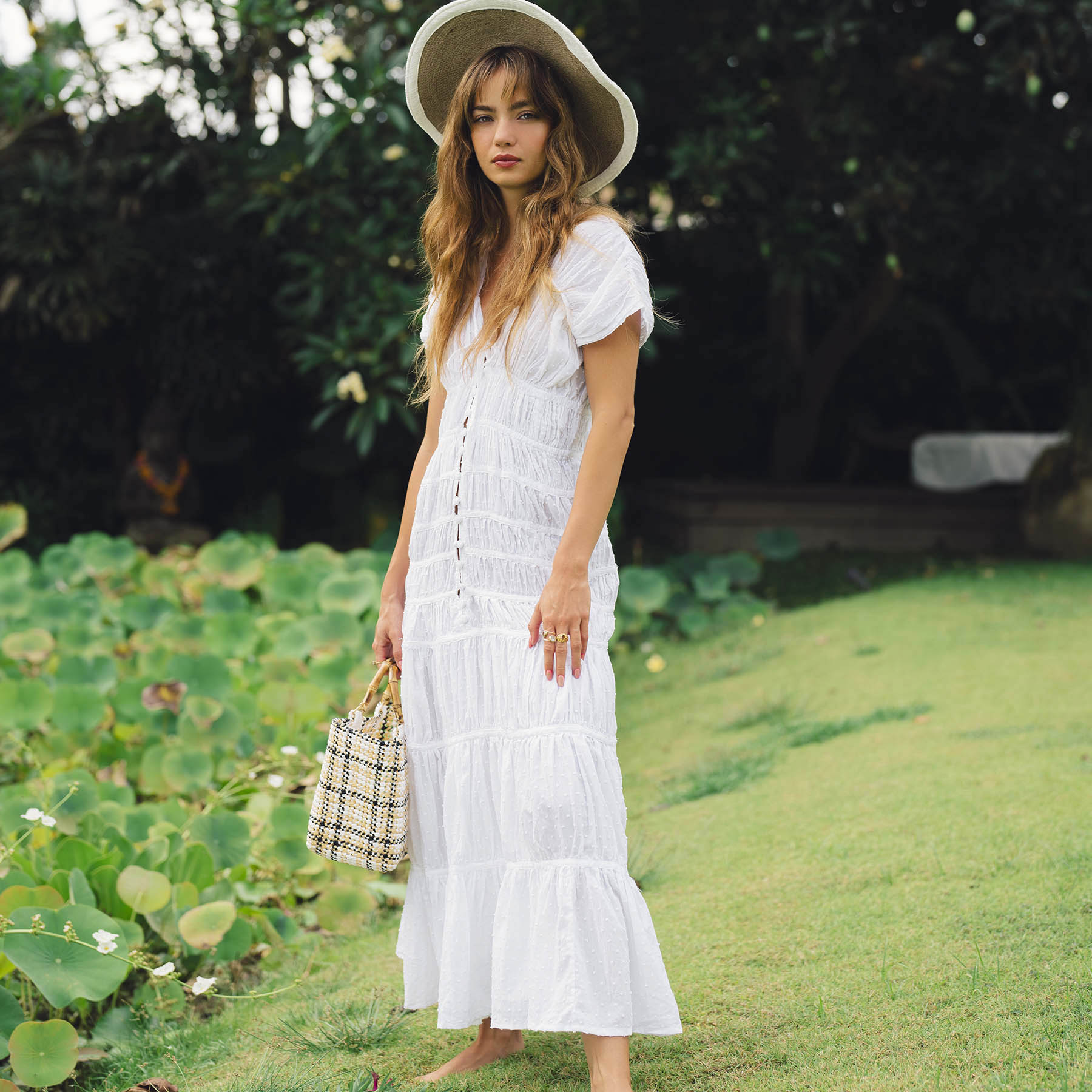 Woman in a white dress and hat standing in a garden