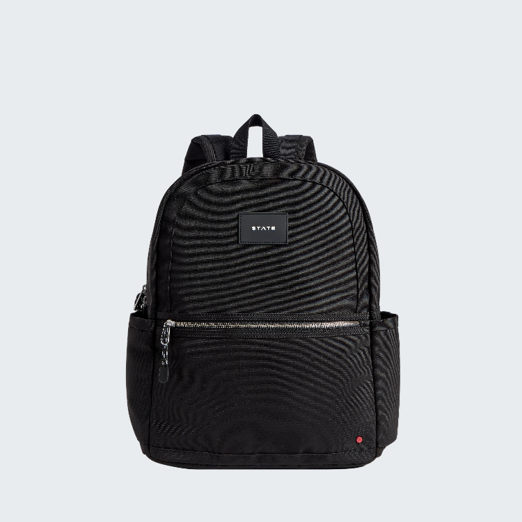 A black canvas backpack with a front zippered pocket and a small rectangular brand patch reading 'STAYS' on the front, shown on a plain white background.