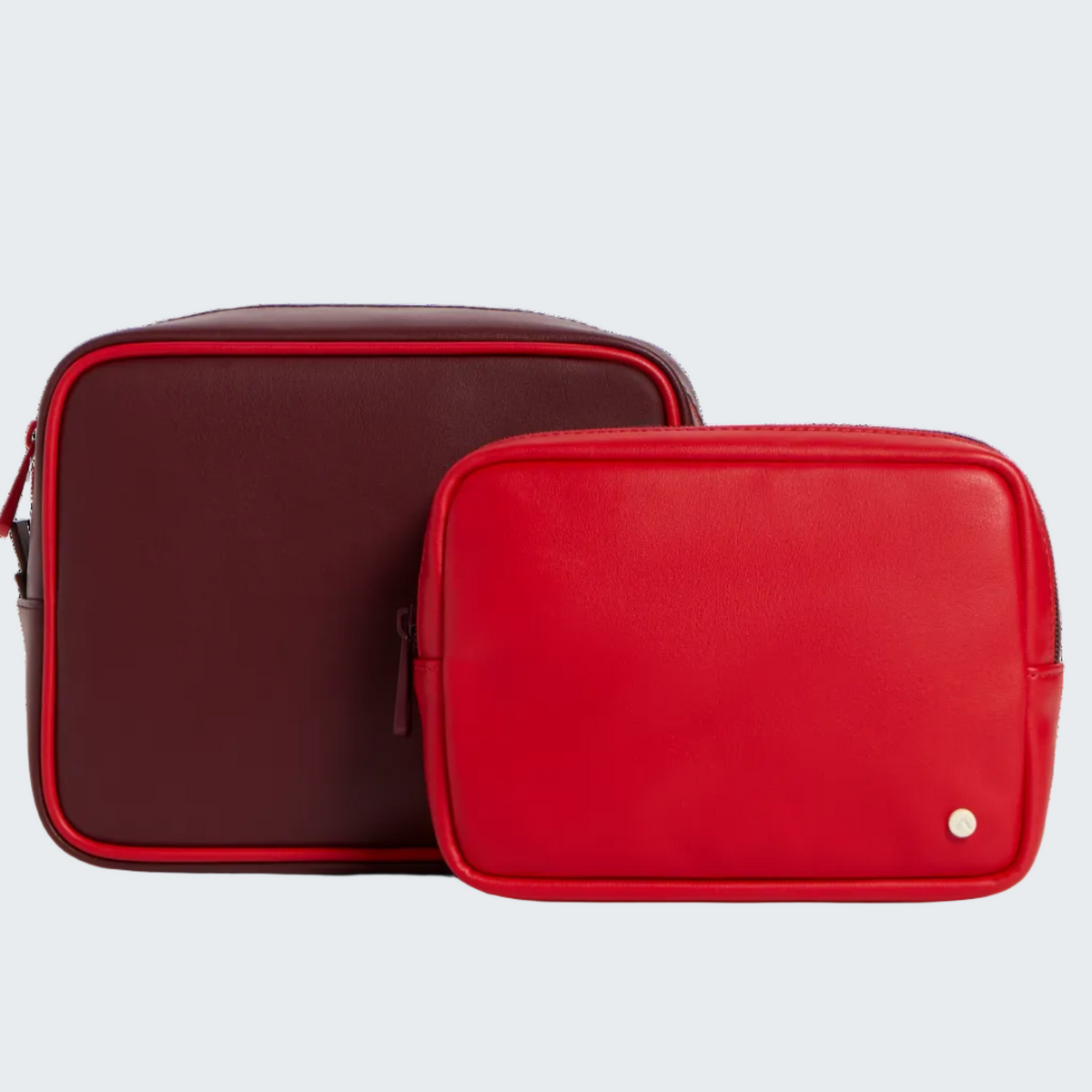 Two rectangular leather zip pouches in red and burgundy, displayed on a clean white background.