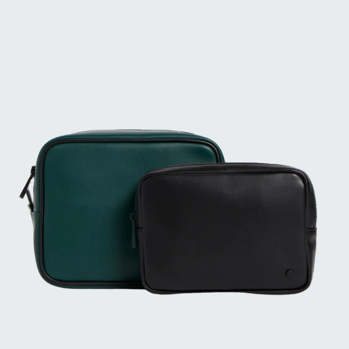 Two rectangular zip pouches or small bags on a clean white studio background, one in dark teal-green and one in black, with the black bag placed in front.