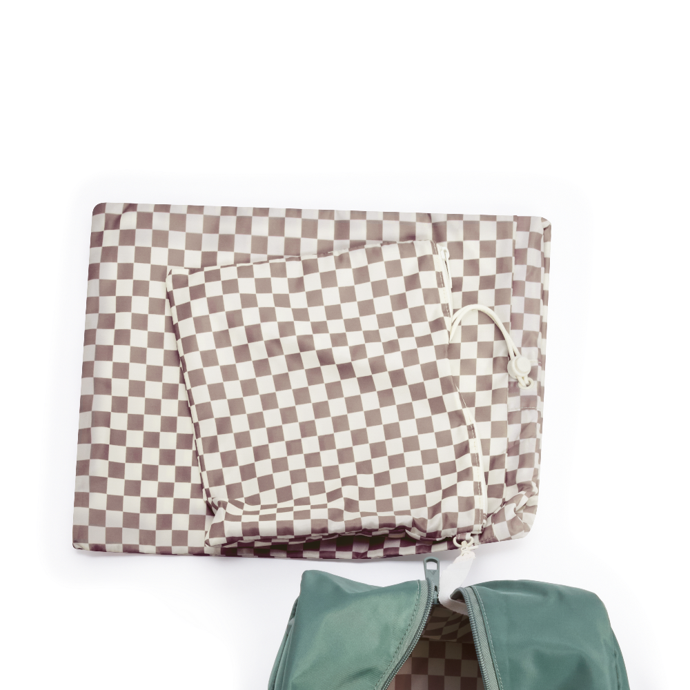 Checkered blanket with a green bag underneath on a white background
