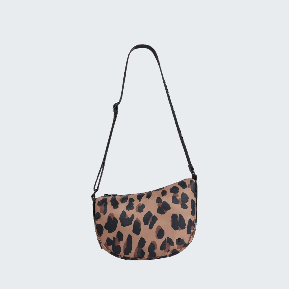 A crescent-shaped shoulder bag with a brown and black leopard print pattern, featuring a black adjustable shoulder strap, shown on a plain white background.