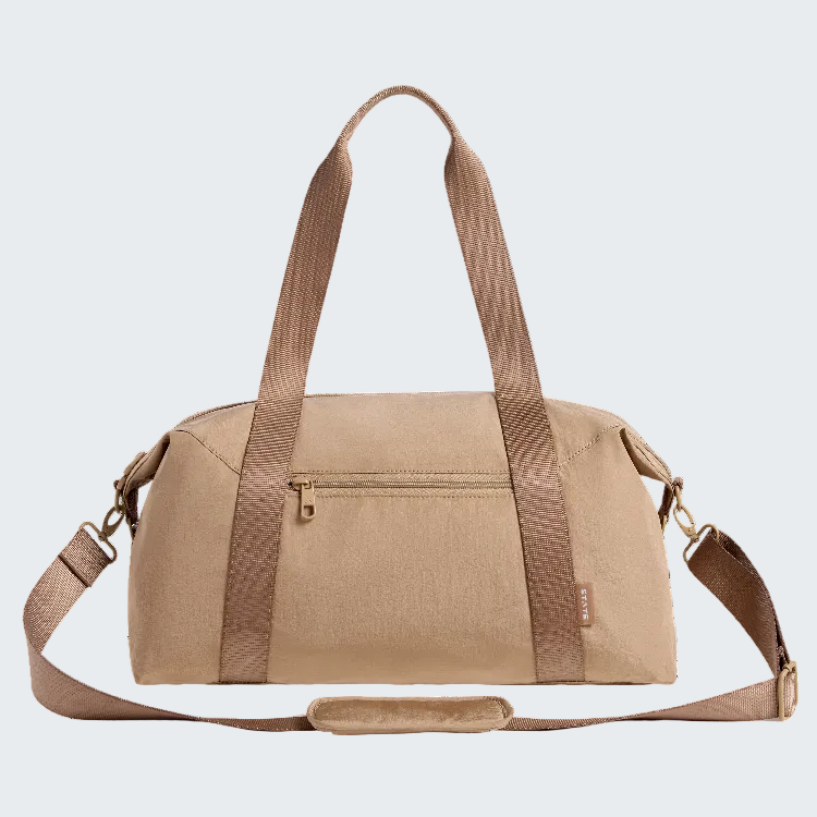 A beige duffel bag with brown handles and shoulder strap, featuring a front zippered pocket and a small vertical brand tag that reads 'SUNRISE'.