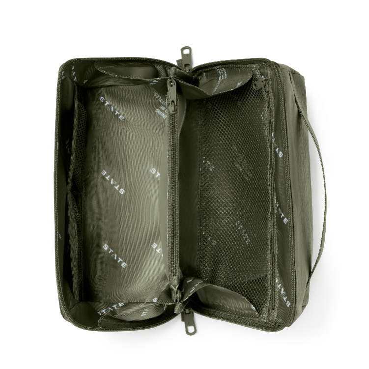 An olive green zippered toiletry bag shown open from a top-down view, revealing a spacious interior with mesh pockets and a repeating white 'STATE' brand print on the lining.
