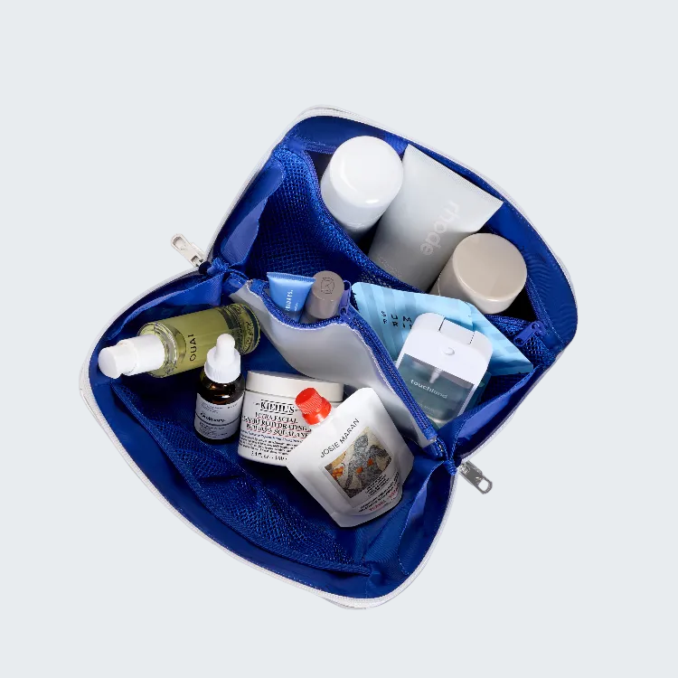 An open blue toiletry bag filled with skincare and beauty products, photographed from above on a plain white background. Visible brands include Kiehl's, The Ordinary, and Zieras.