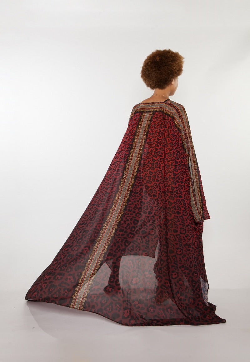 Person wearing a long, patterned dress with a sheer overlay on a white background
