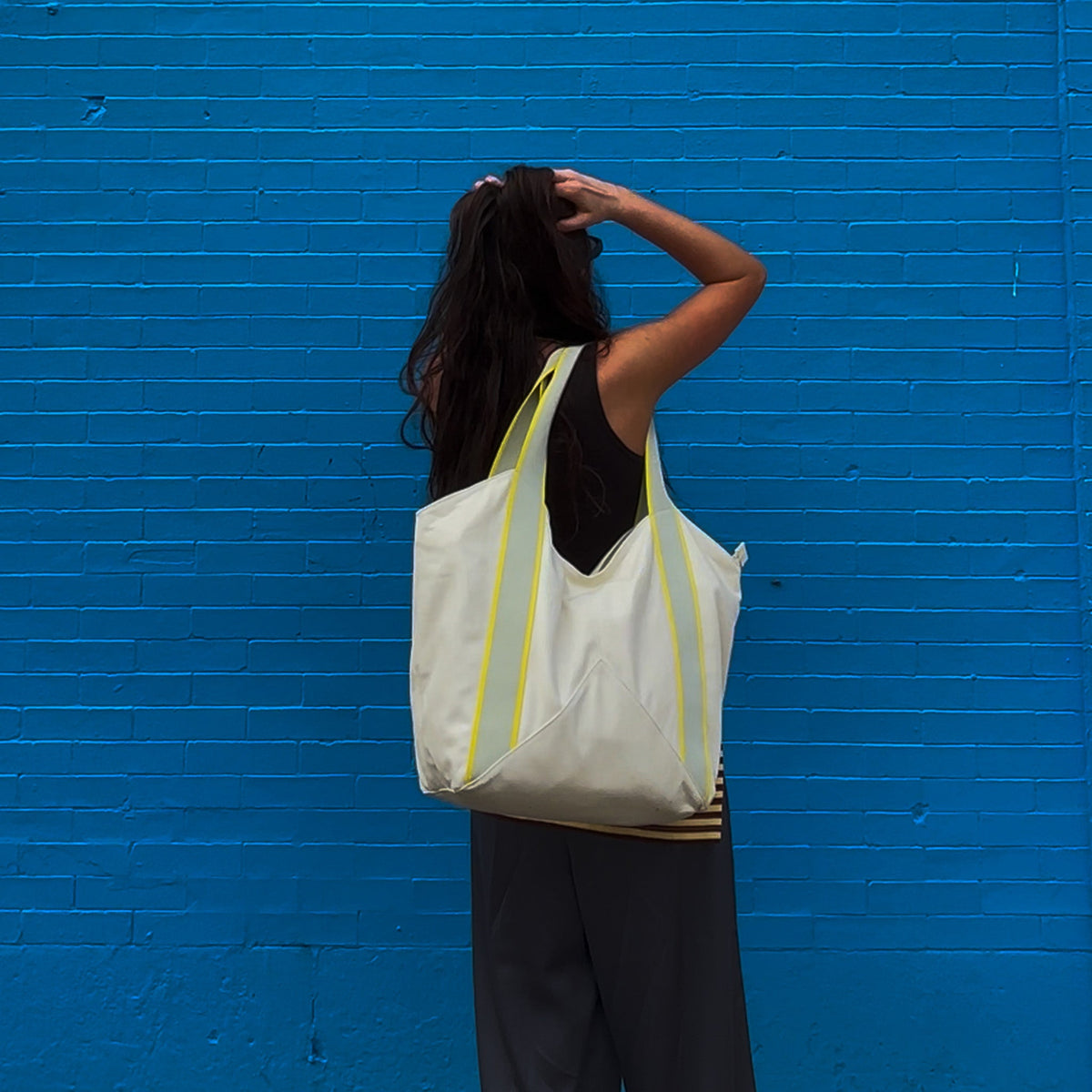 Person with a white tote bag against a blue brick wall