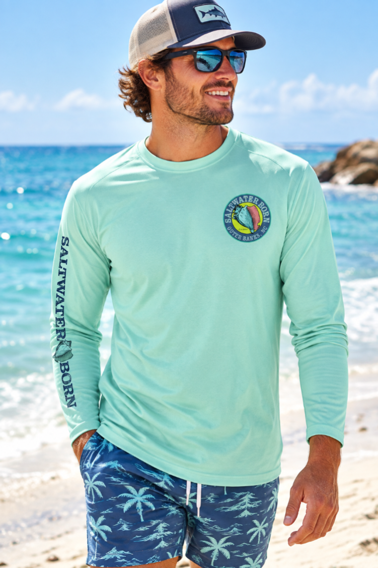 A mint green long-sleeve performance shirt with a circular 'Salvatore's Upper Sands 50' logo on the left chest and 'SALTSVATERS BORN' printed vertically on the right sleeve.