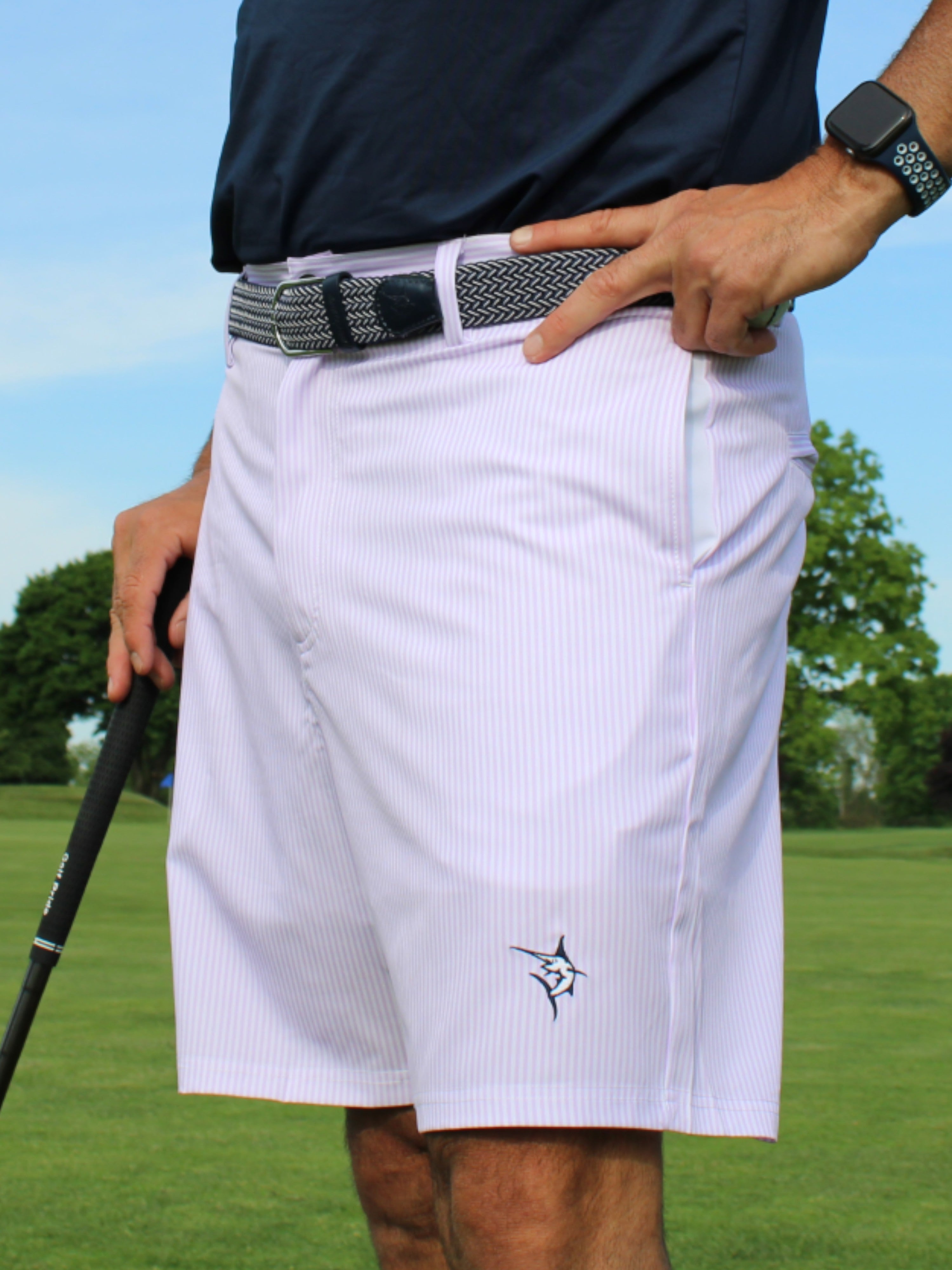 Person wearing white golf shorts with a logo on a golf course