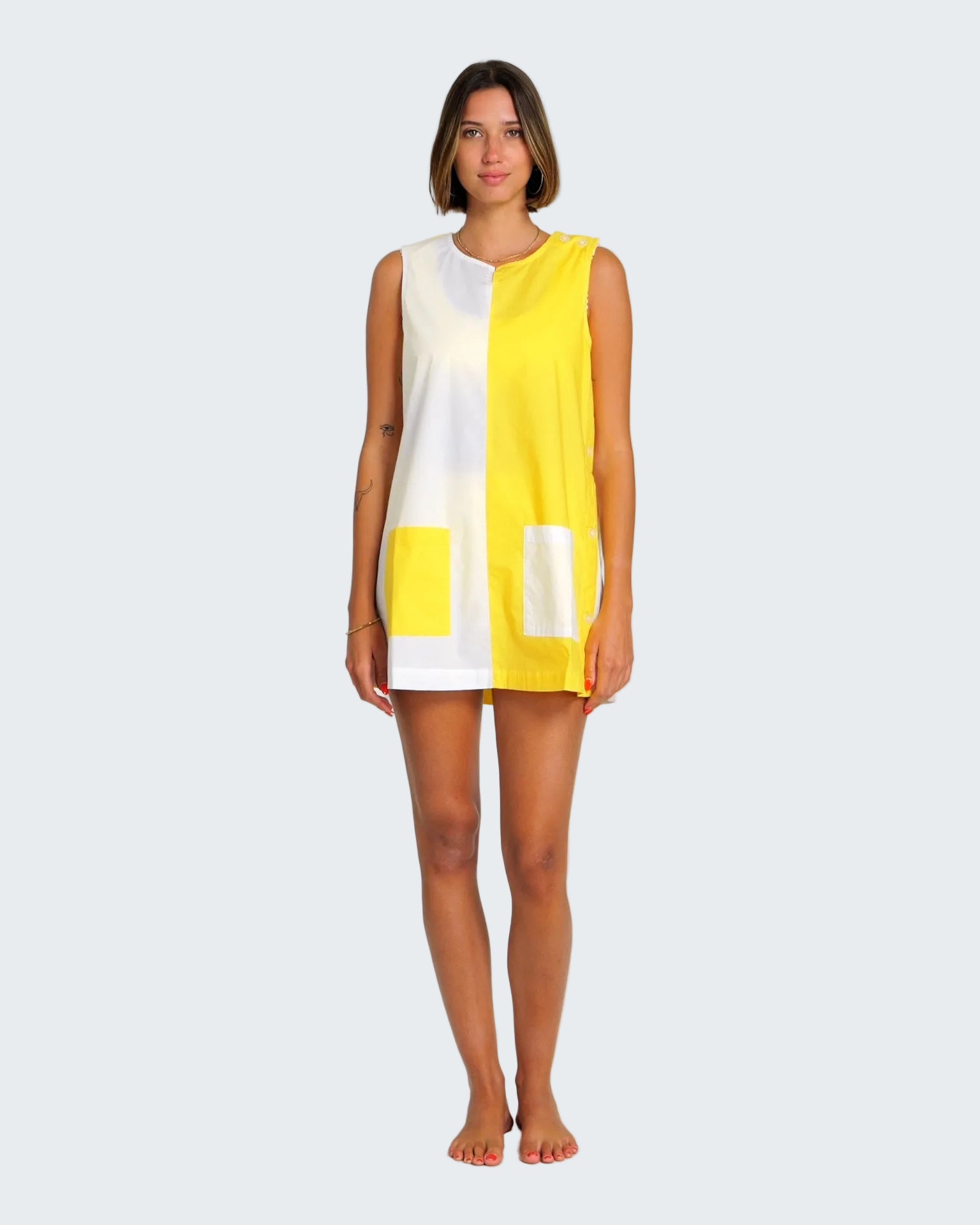 Woman wearing a yellow and white sleeveless dress on a plain background