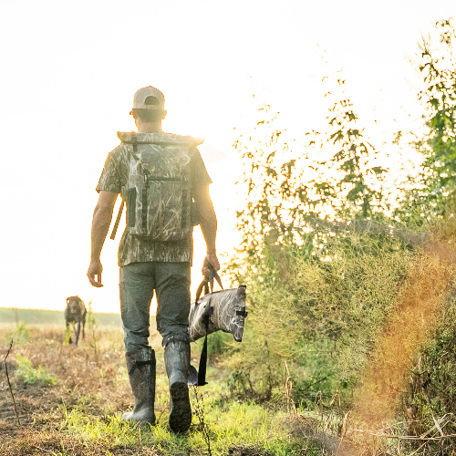 Man in camouflage walking through a field with a horse in the background