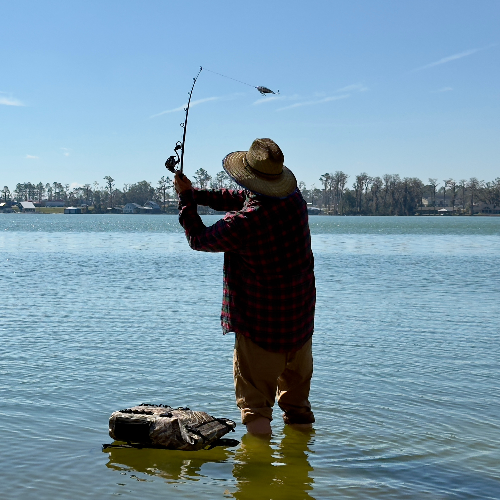 Person fishing in a lake with a clear blue sky