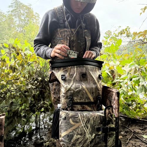 Person in camouflage gear holding a device in a forest setting