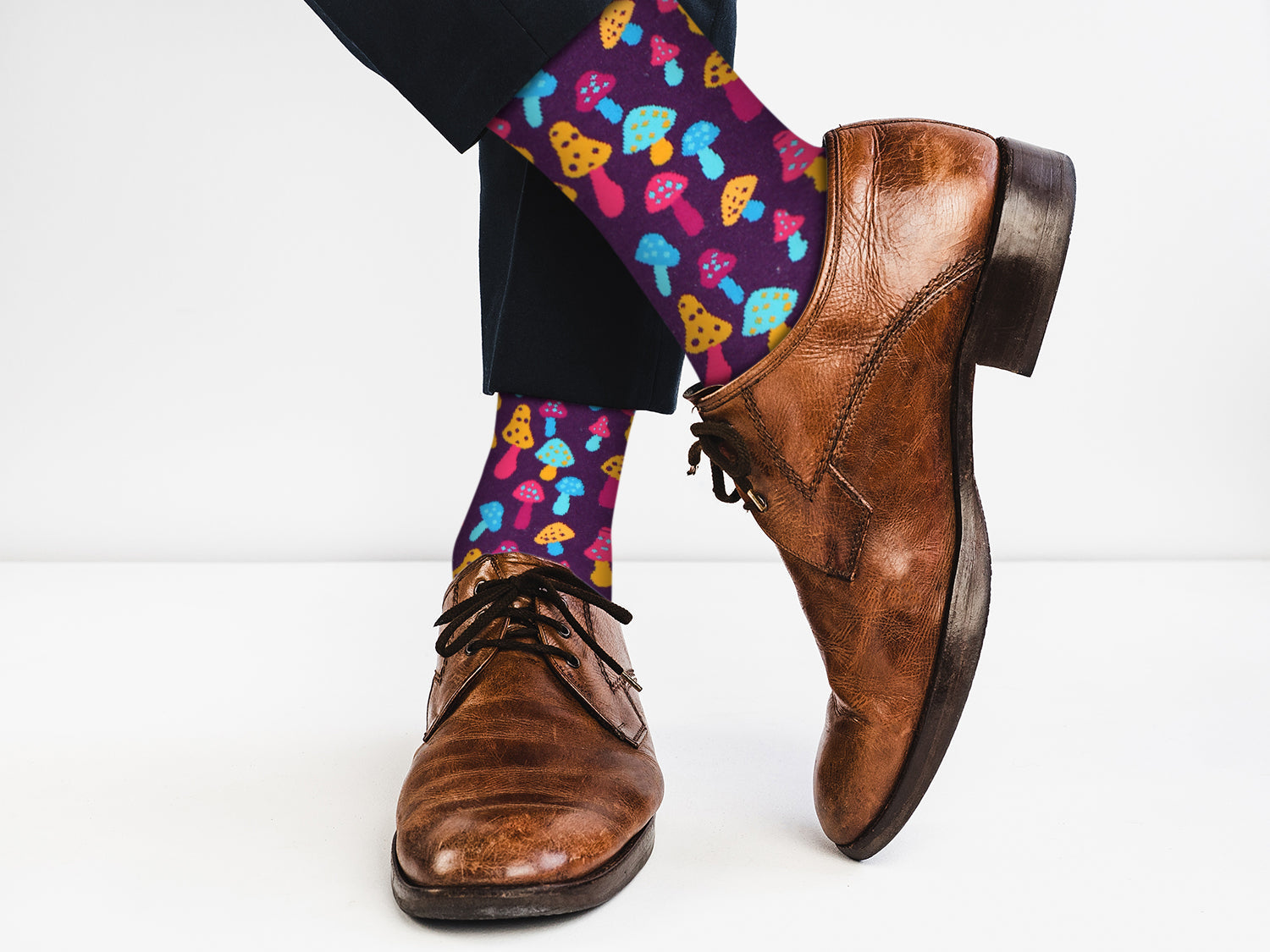 Colorful mushroom-patterned socks with brown dress shoes on a white background