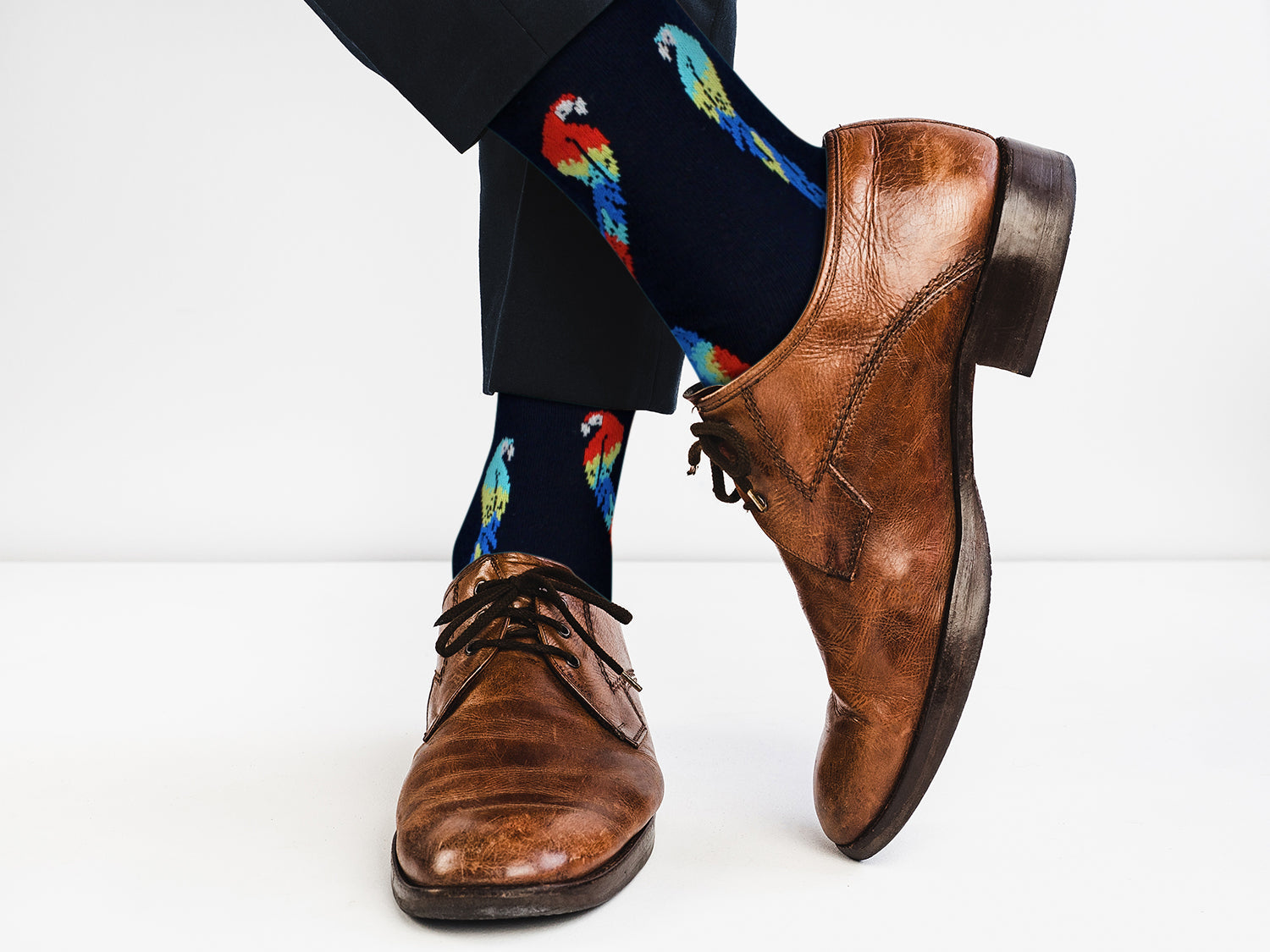 Brown dress shoes and colorful parrot-patterned socks on a white background