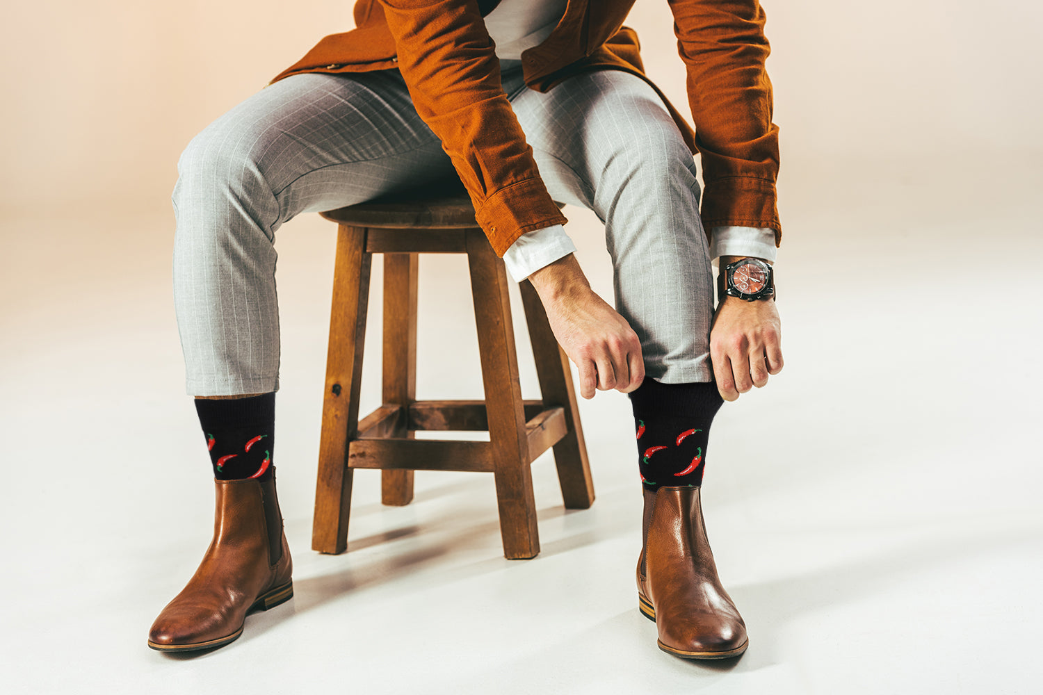 Person wearing brown boots, light gray pants, and a brown jacket sitting on a wooden stool.