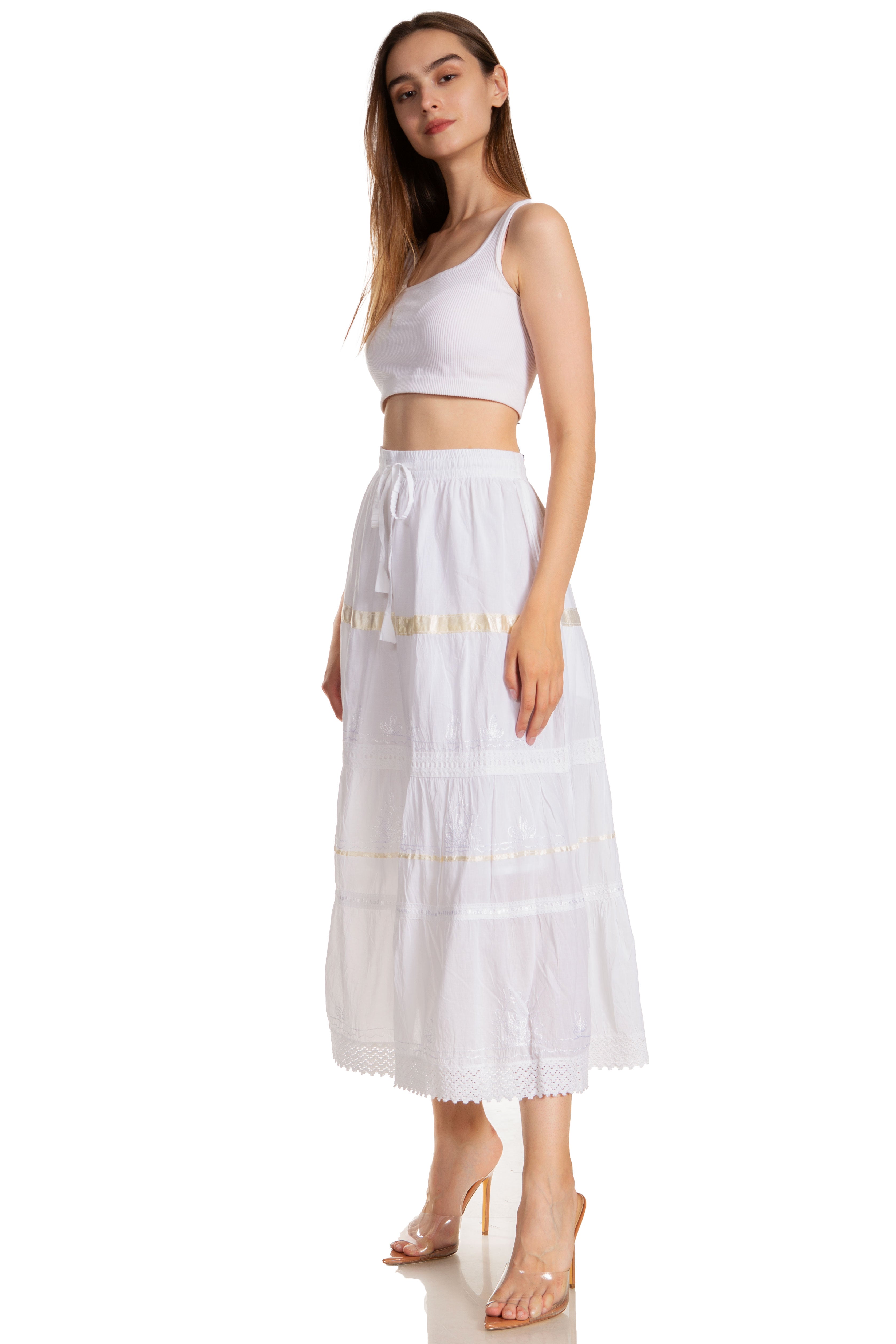 Woman wearing a white sleeveless top and long white skirt with gold trim on a white background