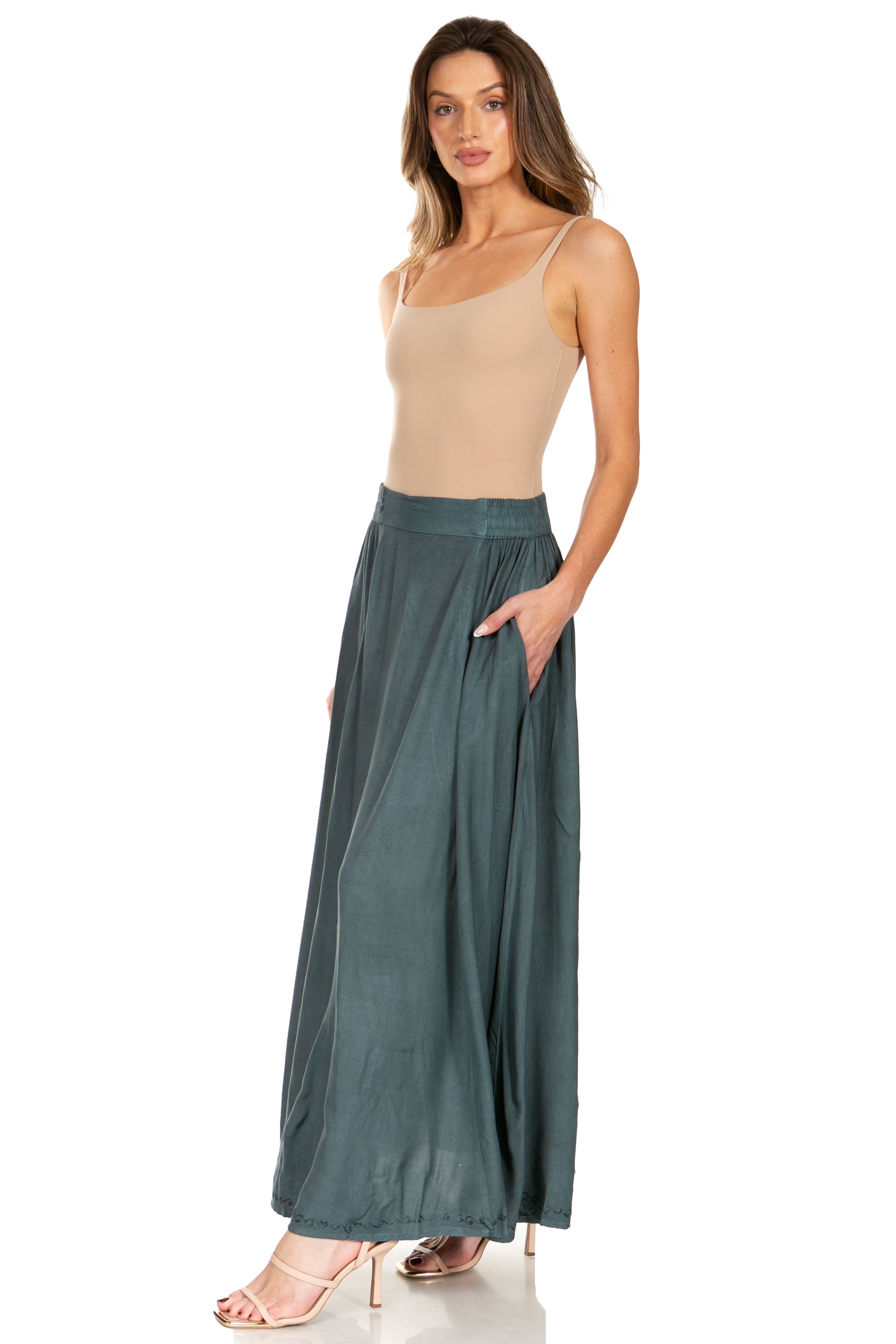 Woman wearing a beige tank top and teal wide-leg pants on a white background
