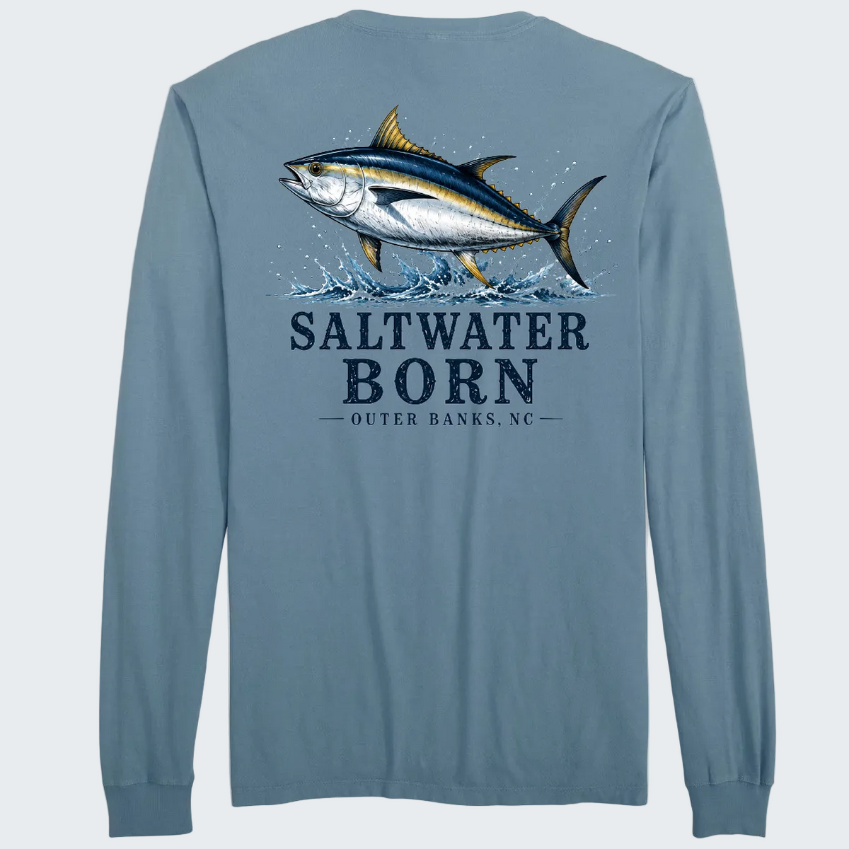 A long-sleeve t-shirt in a dusty slate blue color, shown from the back. The back features a large graphic print of a tuna fish jumping out of water, with the text 'SALTWATER BORN' and 'OUTER BANKS, NC' printed below in navy blue.