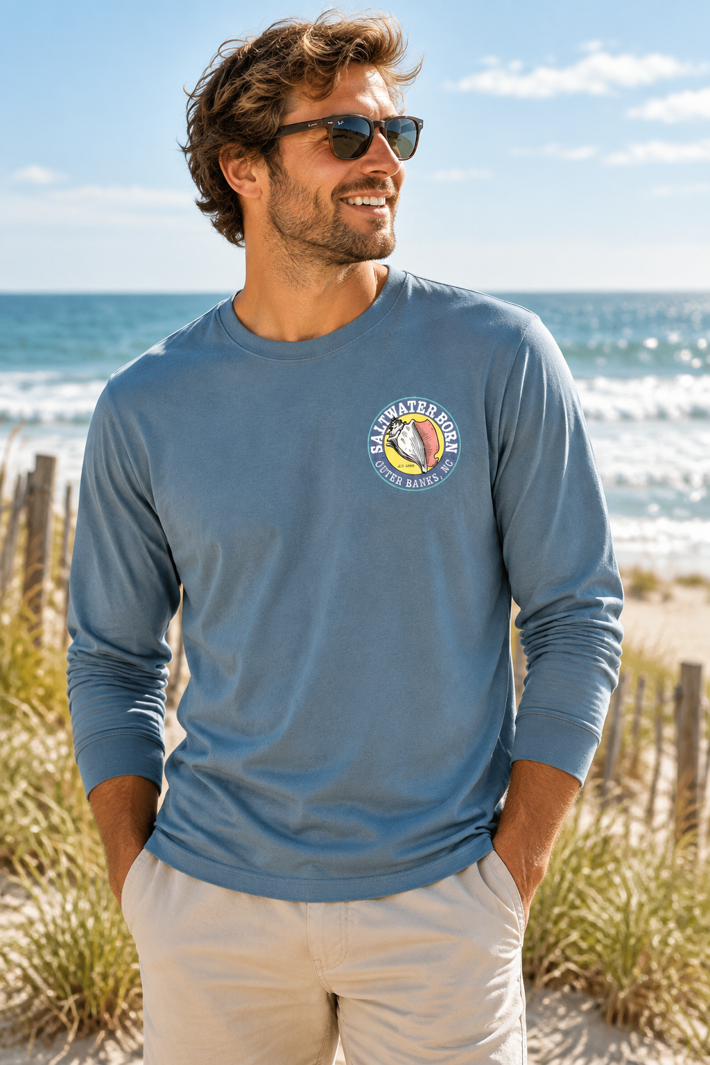 A dusty blue long-sleeve t-shirt with a circular 'Salt Water Dog Outer Base Club' graphic printed on the left chest, displayed on a clean white background.
