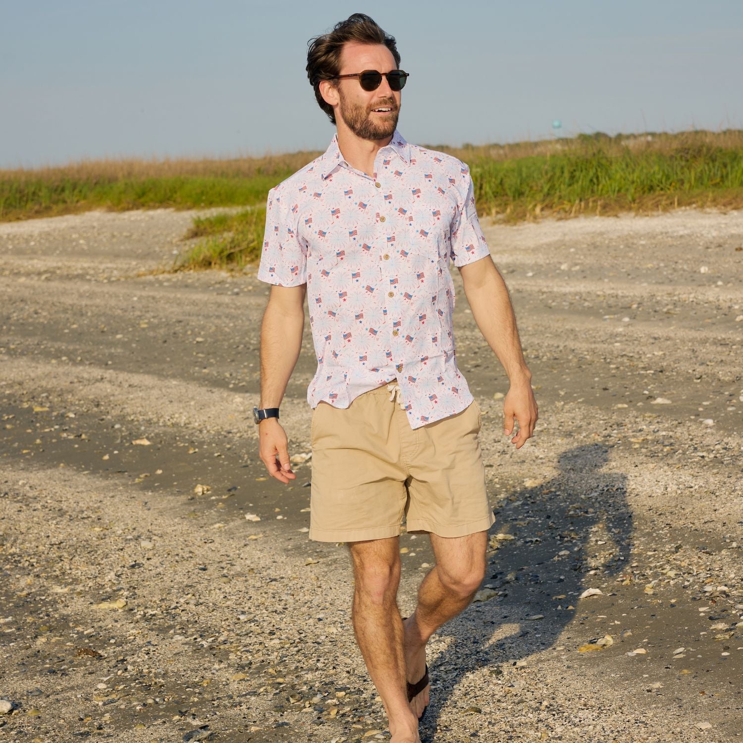 Man walking outdoors on a gravel path with grass and clear sky in the background