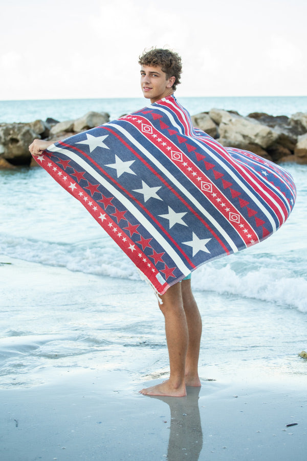 Person holding a red, white, and blue patterned towel on a beach.