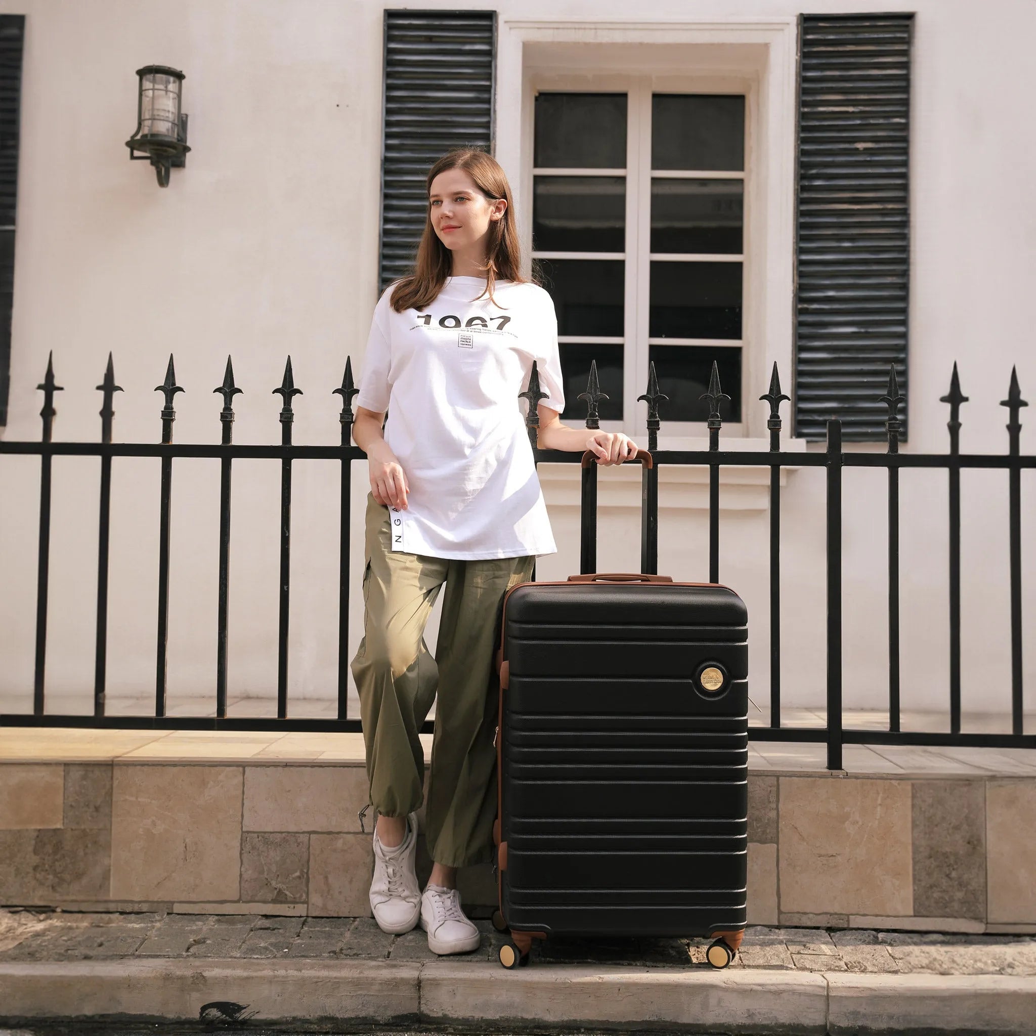 Woman holding a black suitcase in front of a building with black shutters.