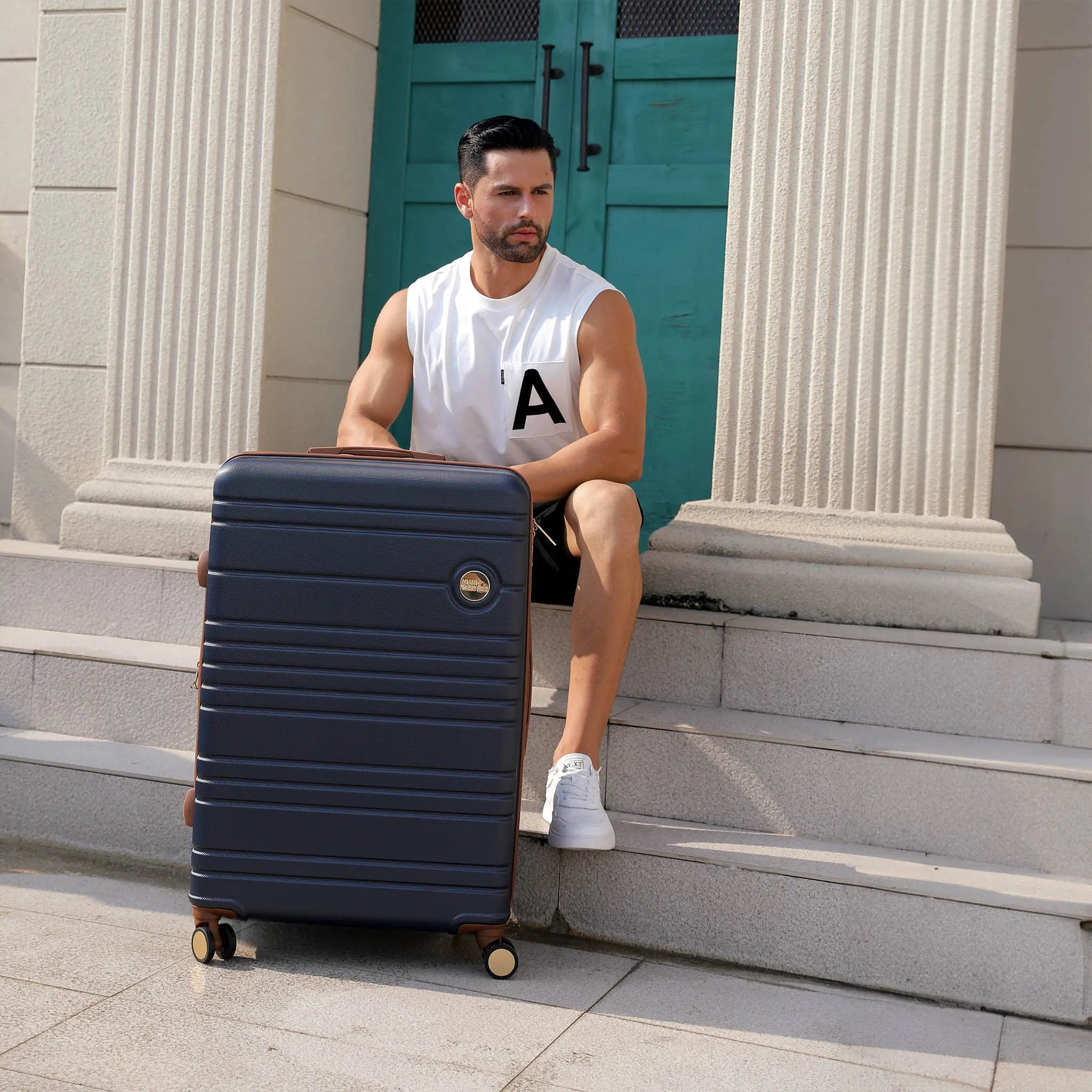 Man sitting on steps with a navy suitcase in front of a building entrance.