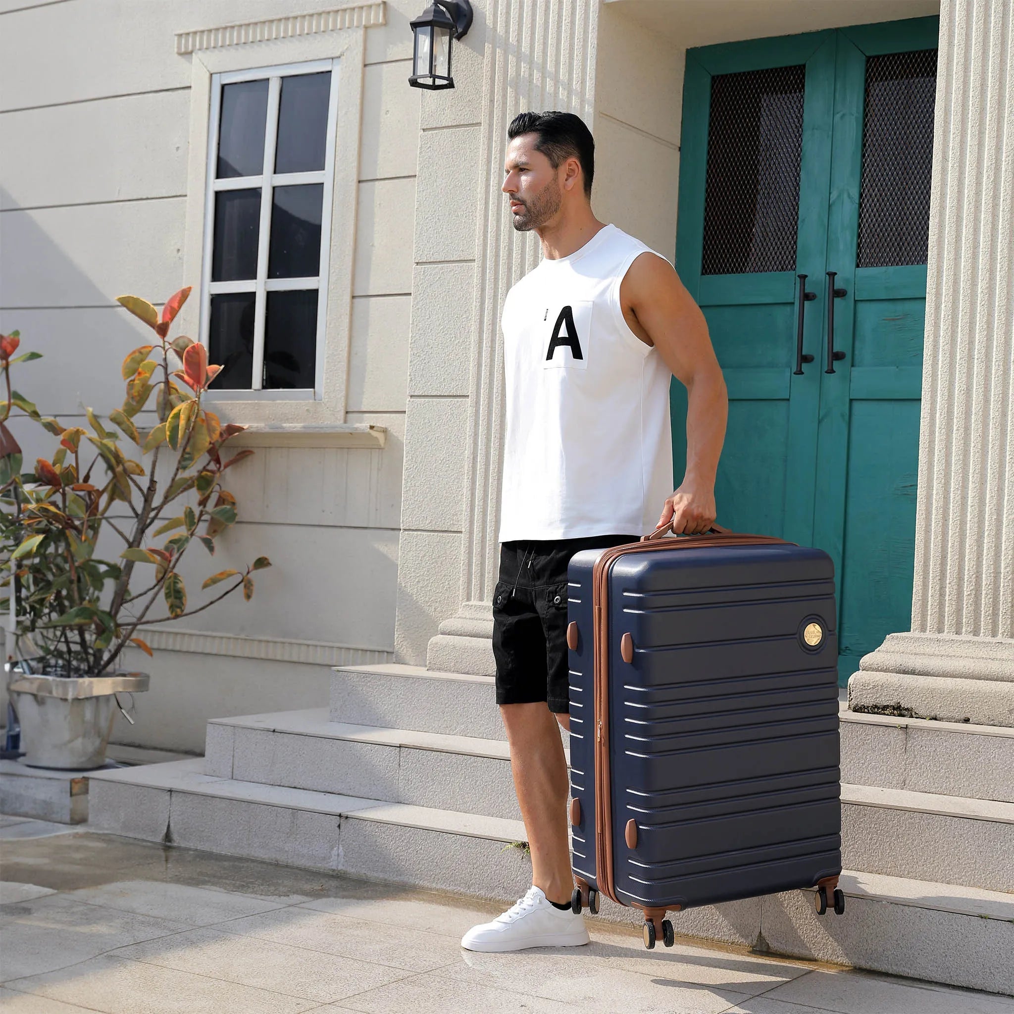 Man holding a navy suitcase outside a house with a teal door.