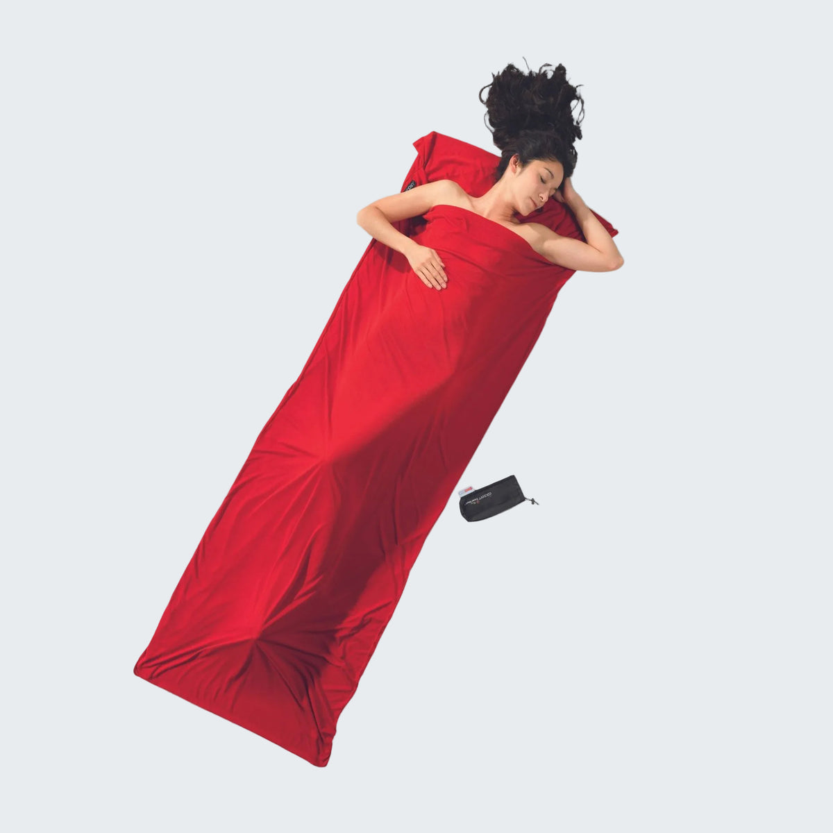 Person lying on a red sleeping bag with a black device next to them on a gray background