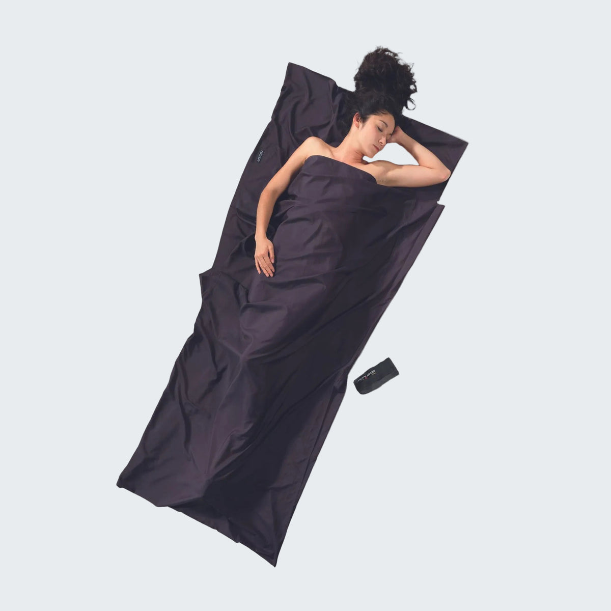 Person lying on a dark purple sleeping bag on a light gray background