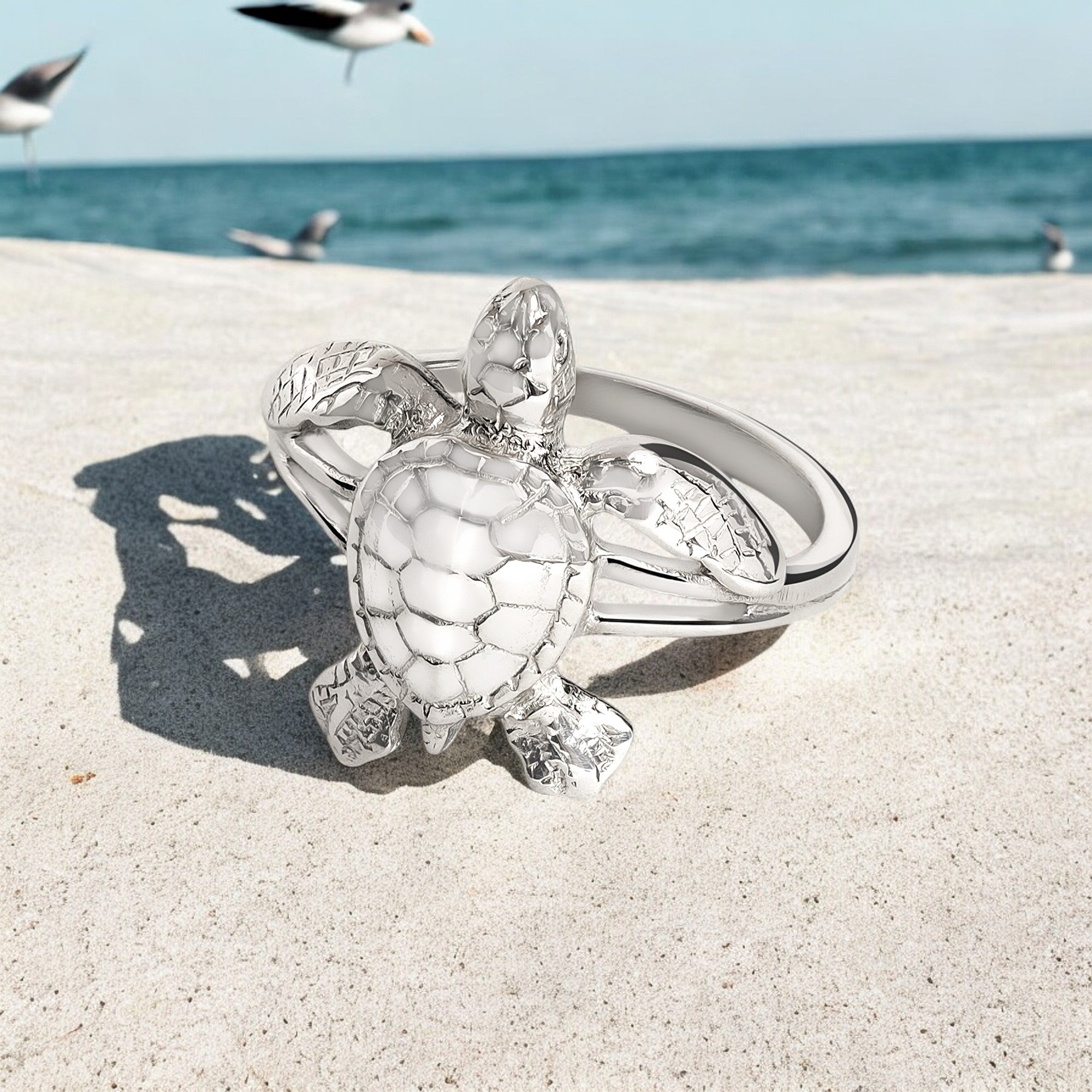 Silver turtle ring on a sandy beach with seagulls in the background