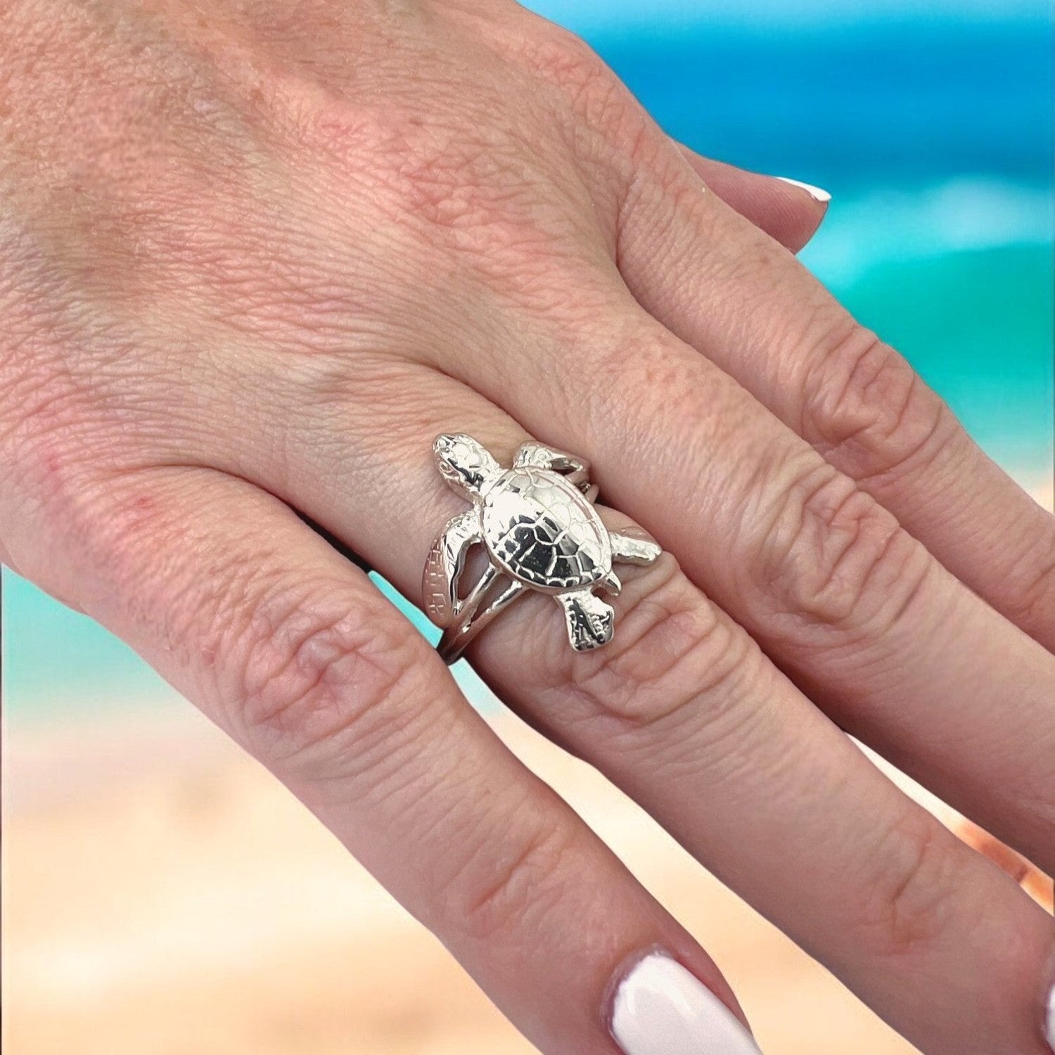 Silver turtle ring on a person's finger with a beach background