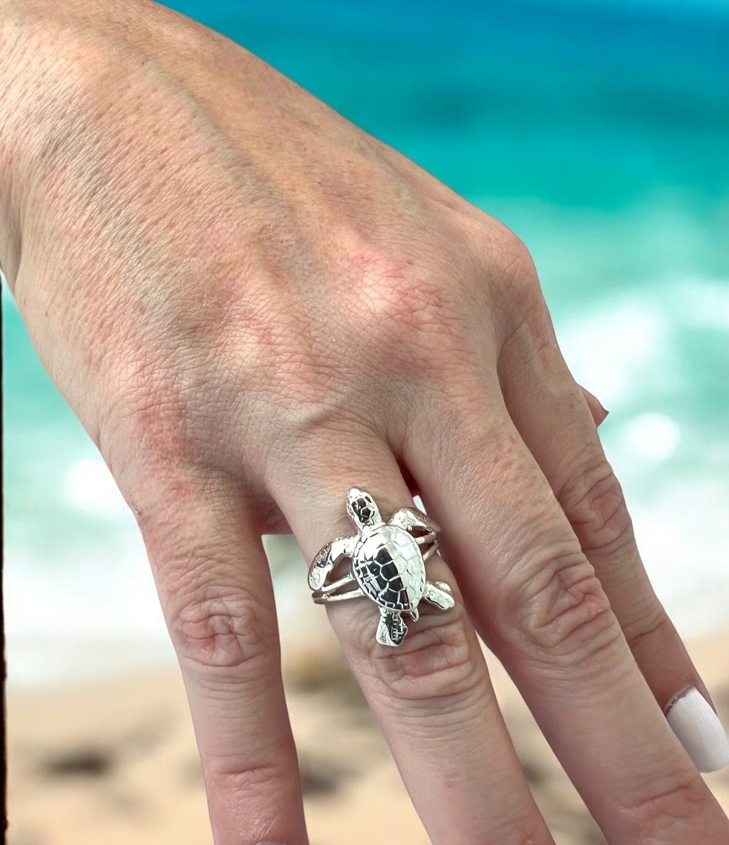 Silver turtle ring on a hand with a beach background