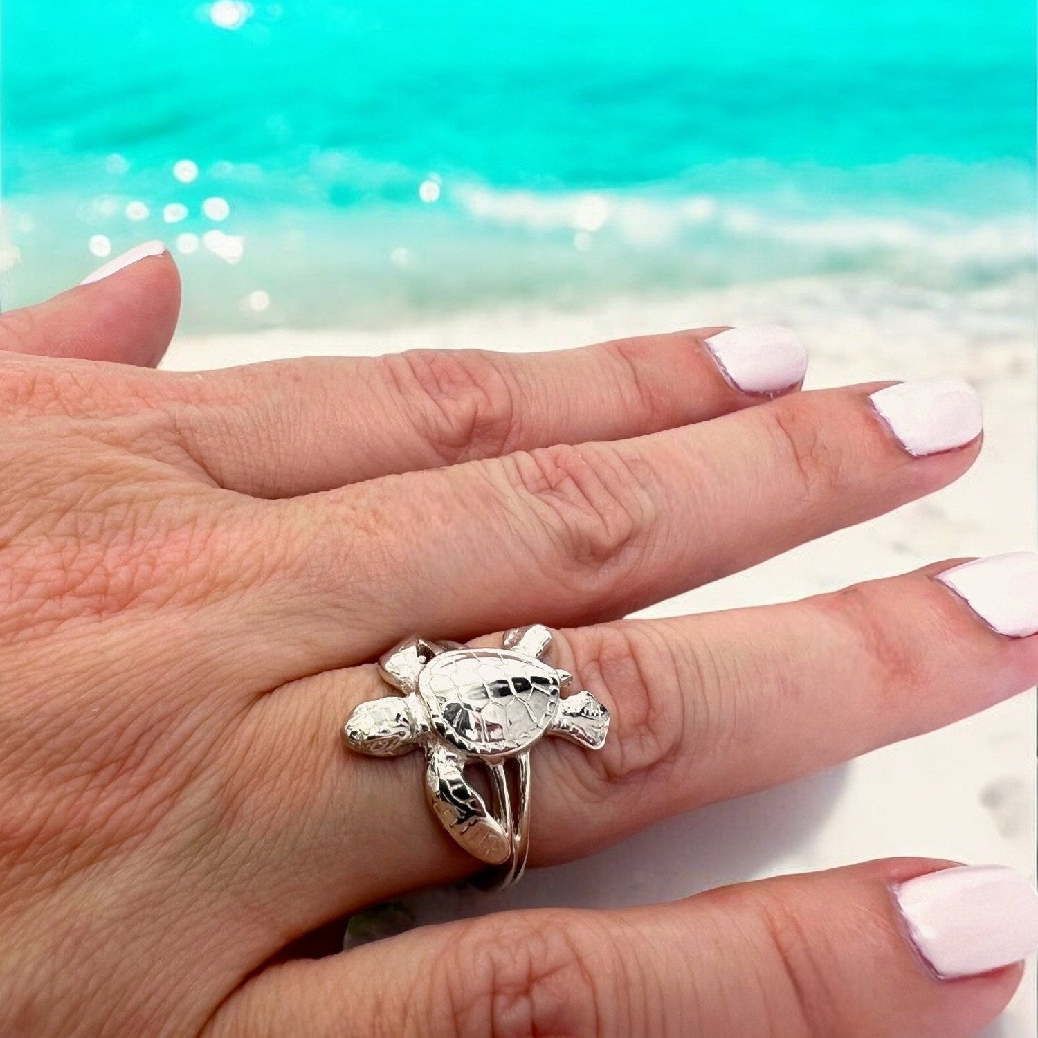 Hand wearing a turtle-shaped ring with a beach background