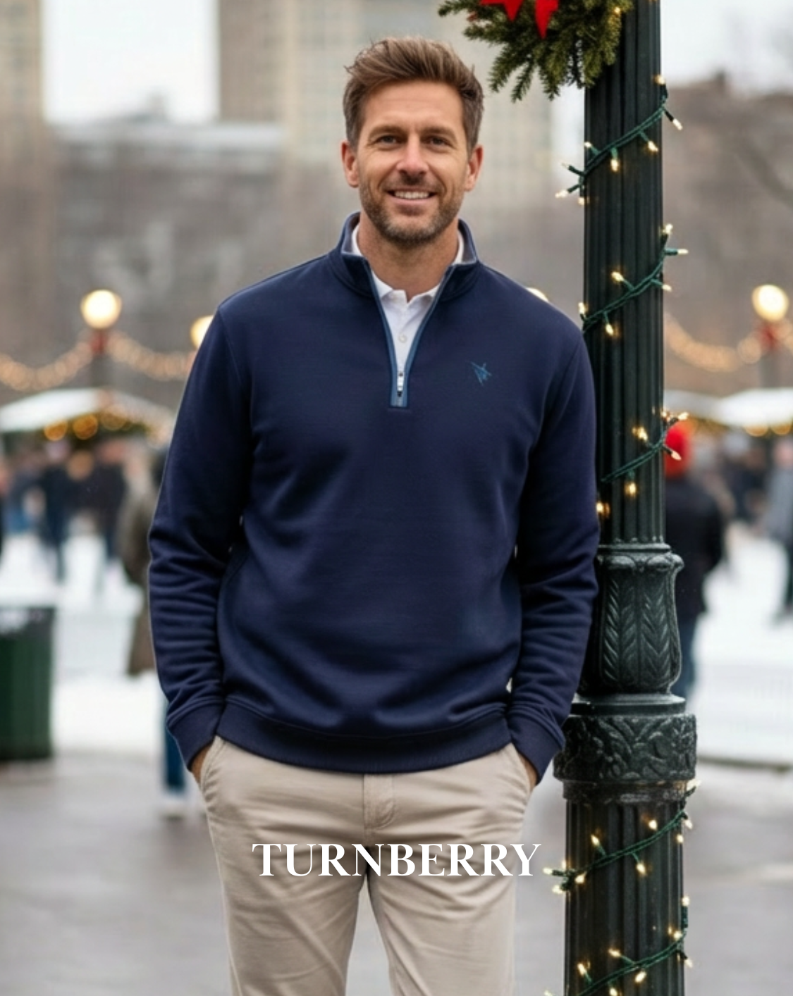 Man wearing a navy blue sweater with a visible brand logo, standing outdoors near festive decorations.