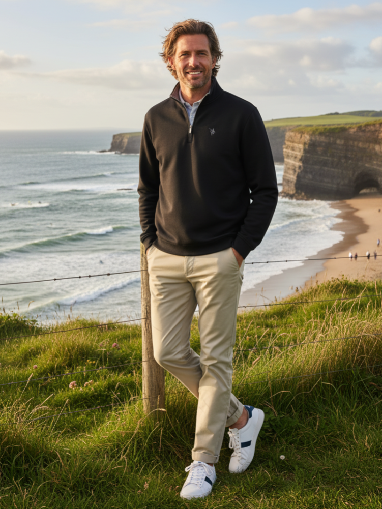 Man standing on a grassy hill overlooking a coastal landscape with cliffs and ocean.