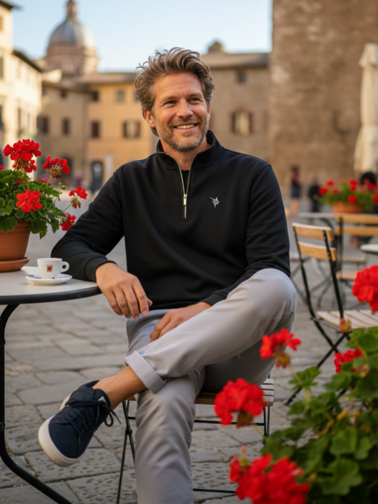 Man sitting outdoors in a scenic location with flowers and buildings in the background