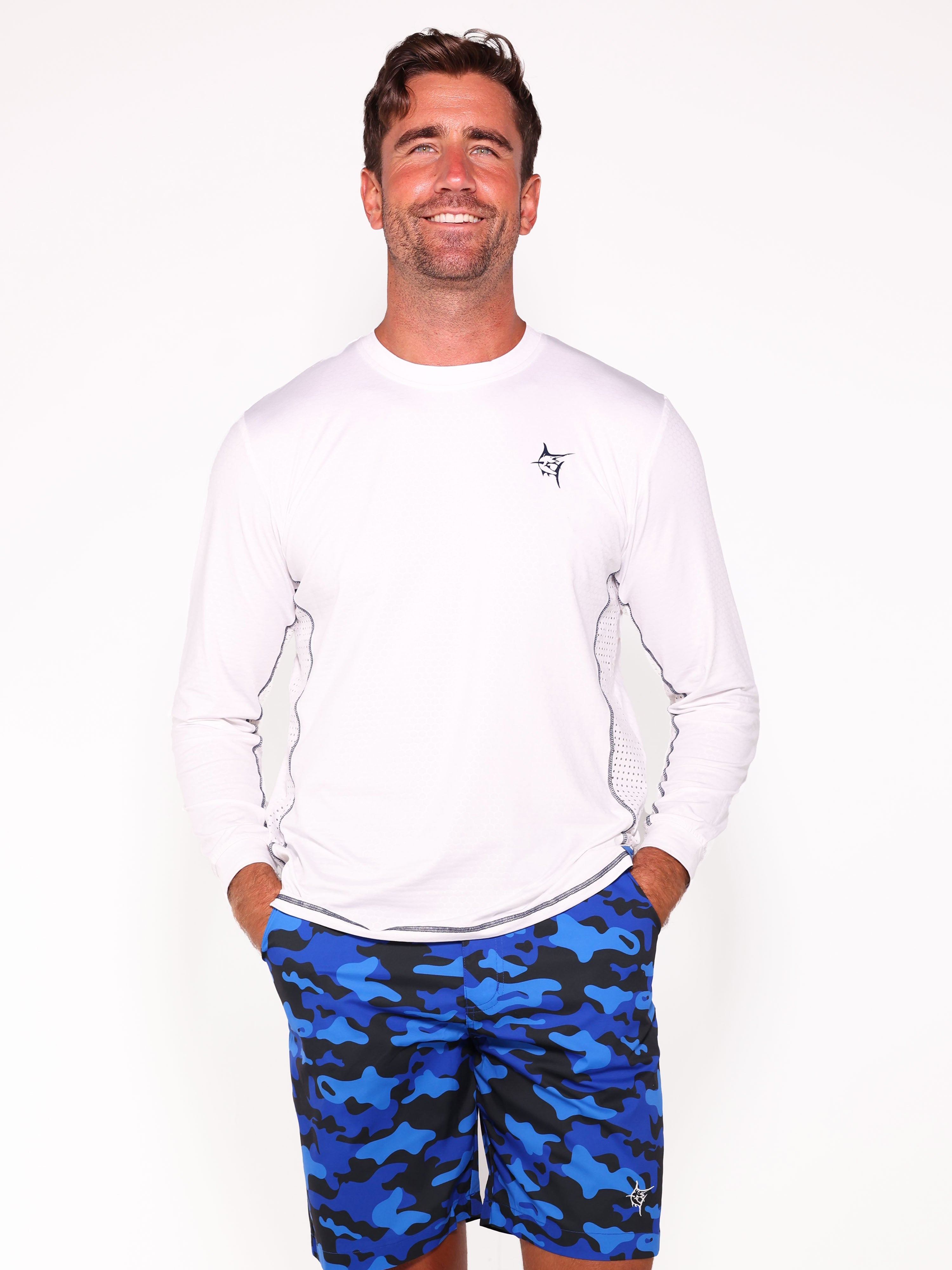Man wearing a white long-sleeve shirt and blue camouflage shorts on a white background
