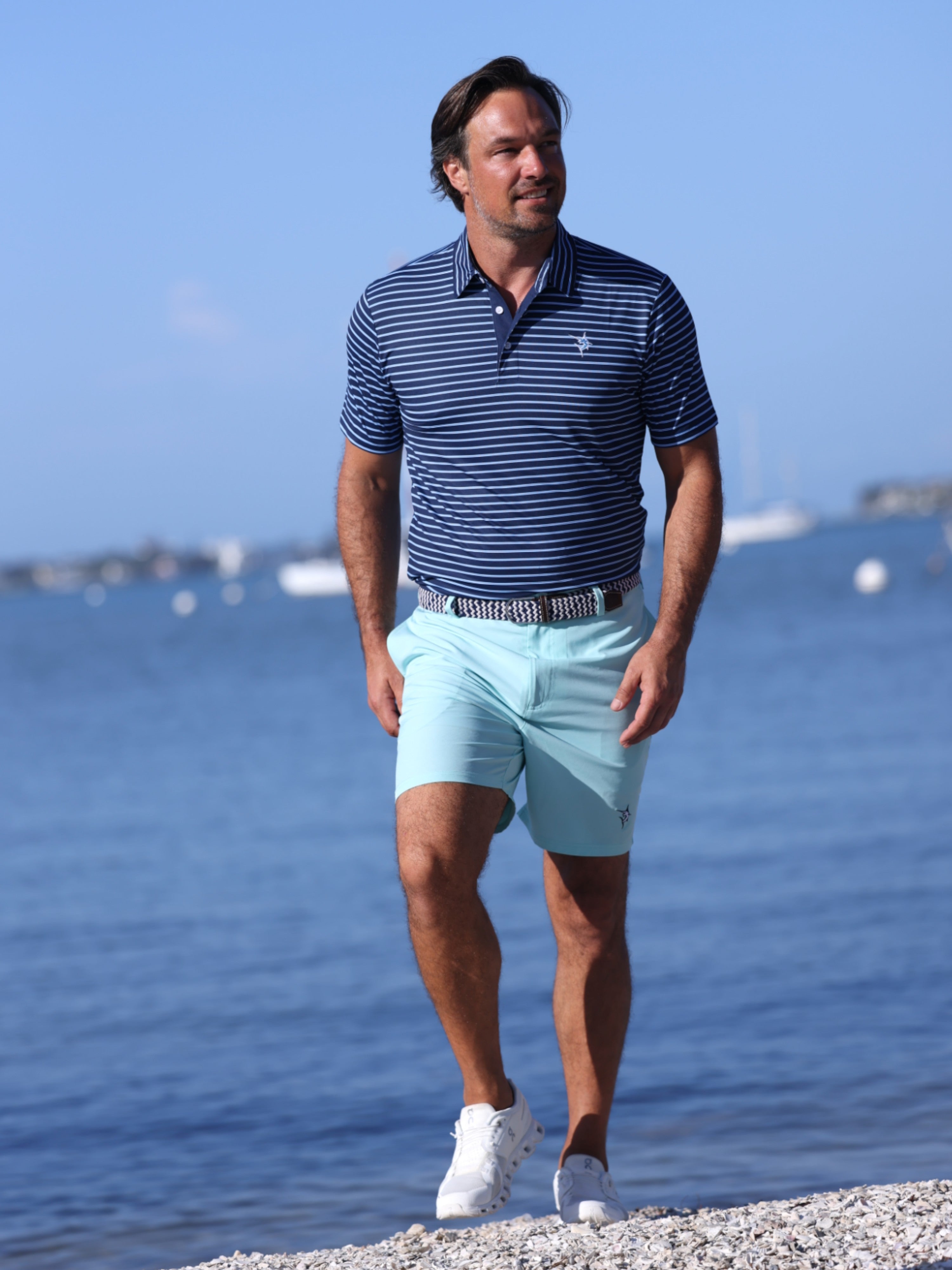 Man in a striped polo shirt and light blue shorts standing by a body of water.