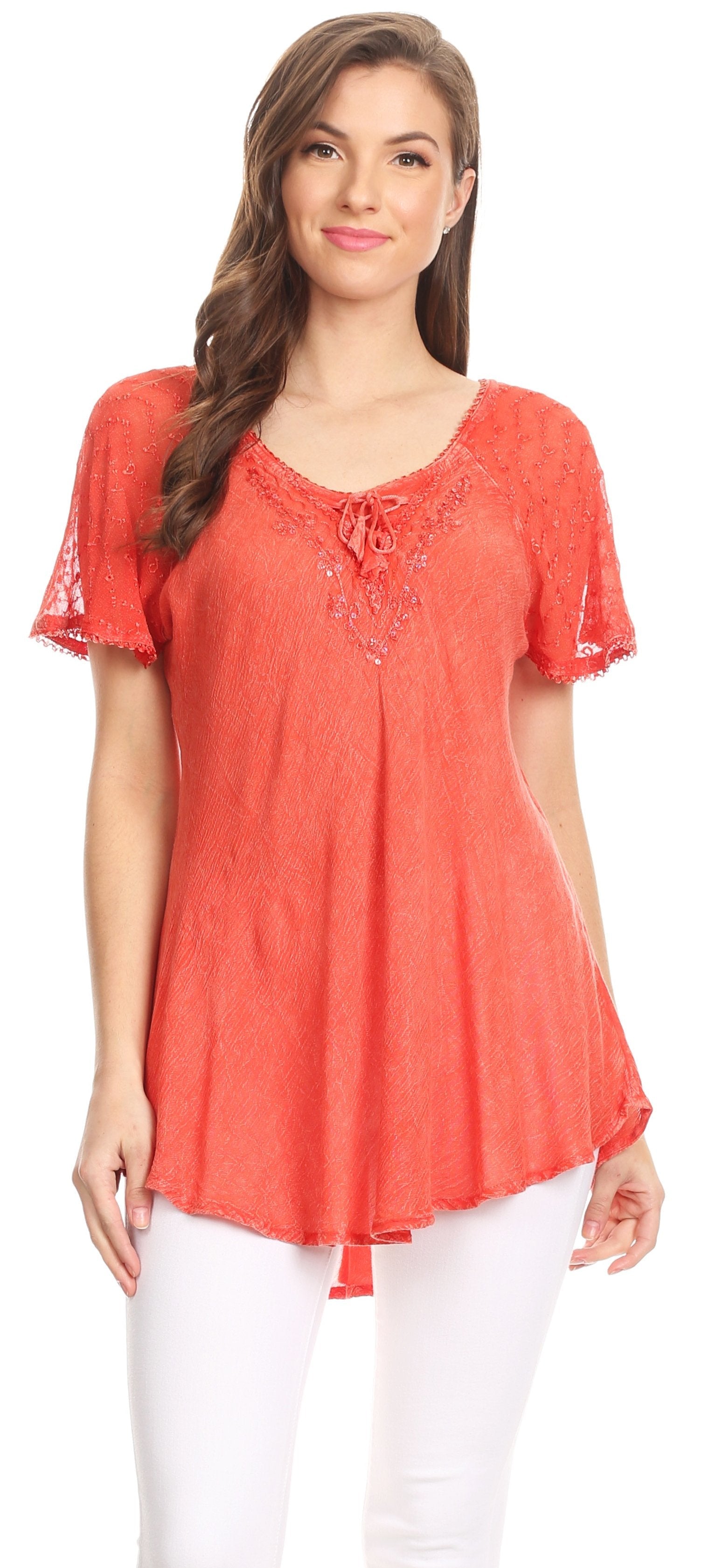 Woman wearing a coral lace-up top with white pants on a plain background